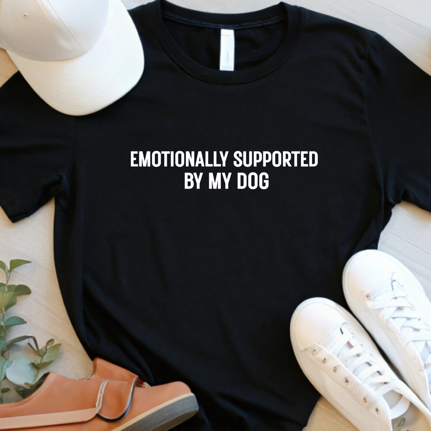 Styled flat lay of black dog lover t-shirt with “Emotionally Supported by My Dog” text and casual accessories