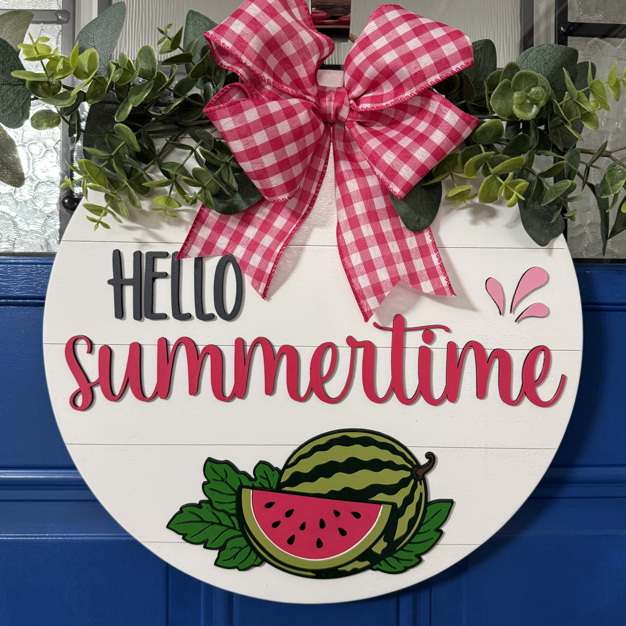 Front view of Hello Summertime watermelon door hanger with raised red lettering, hand-painted watermelon, and red gingham bow on blue door