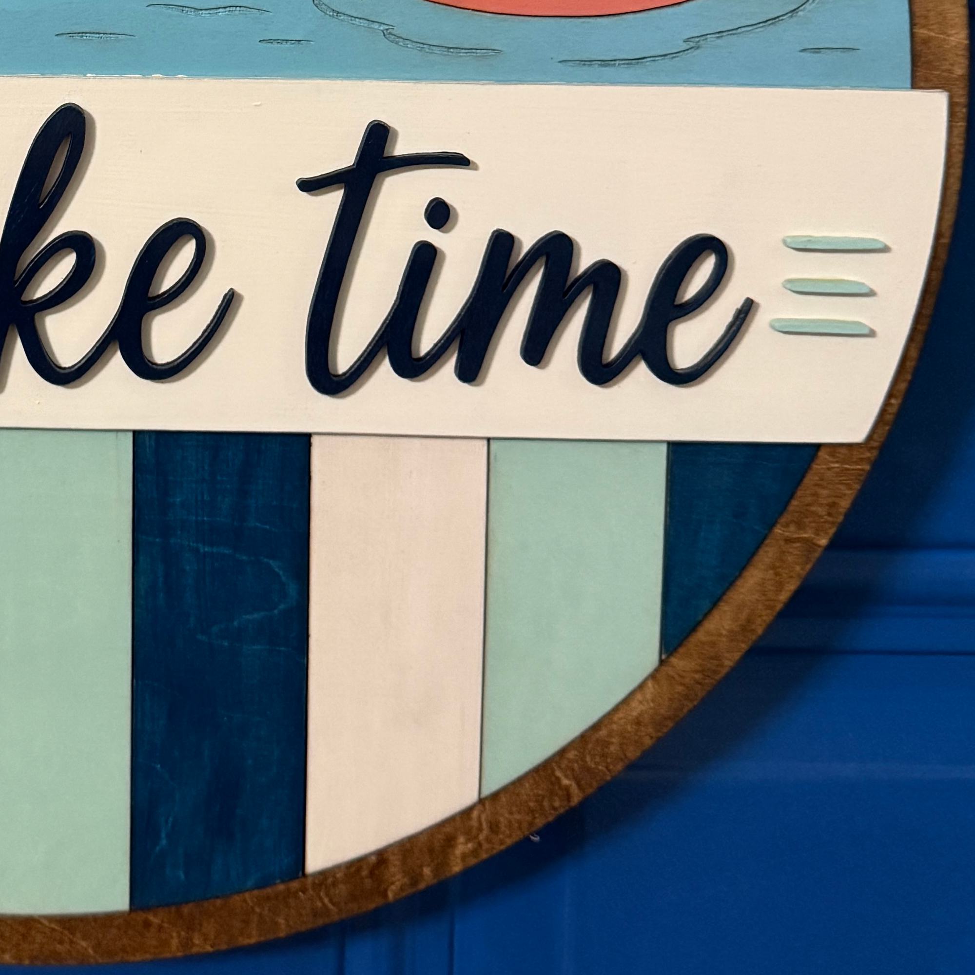 Detail of dimensional lettering and coastal-inspired striped lower section of the lake-themed door hanger.