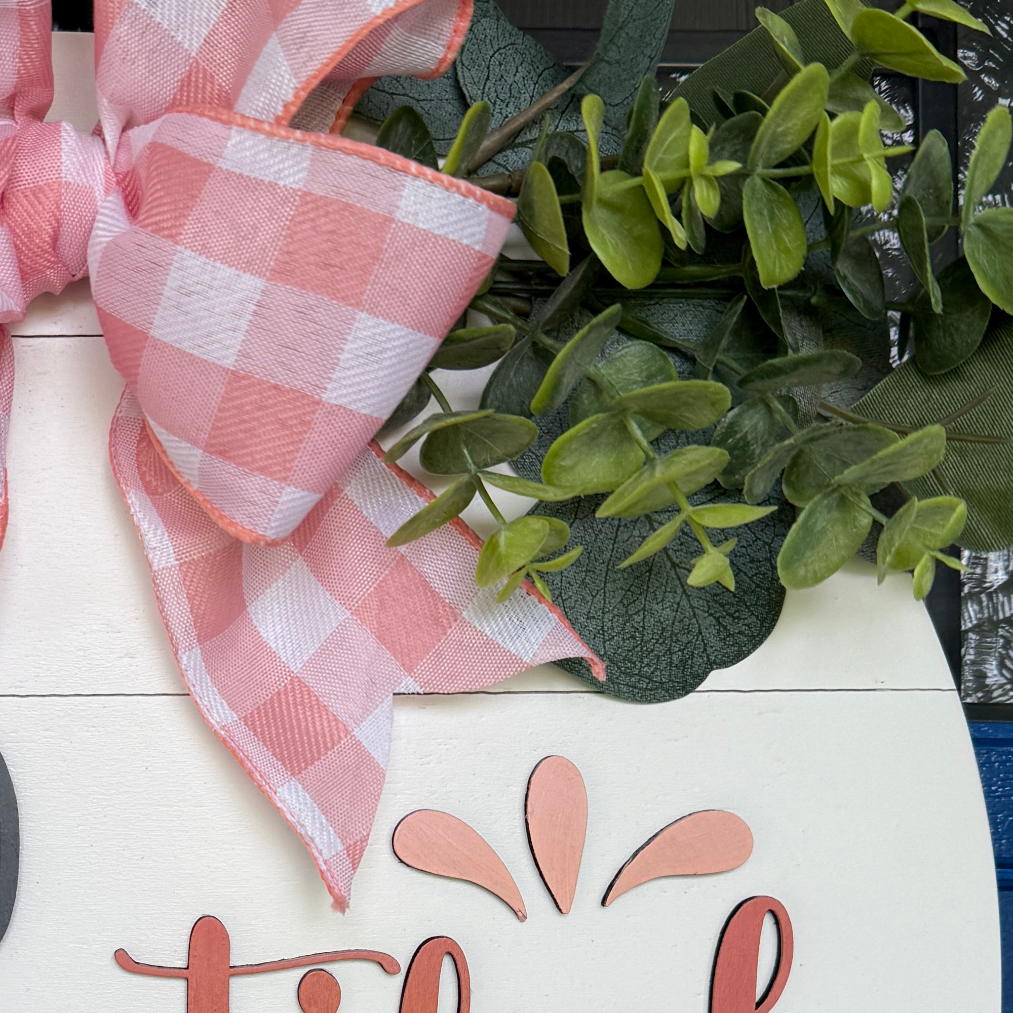 Detail view of eucalyptus greenery and decorative flourish accents on a handcrafted peach door hanger.