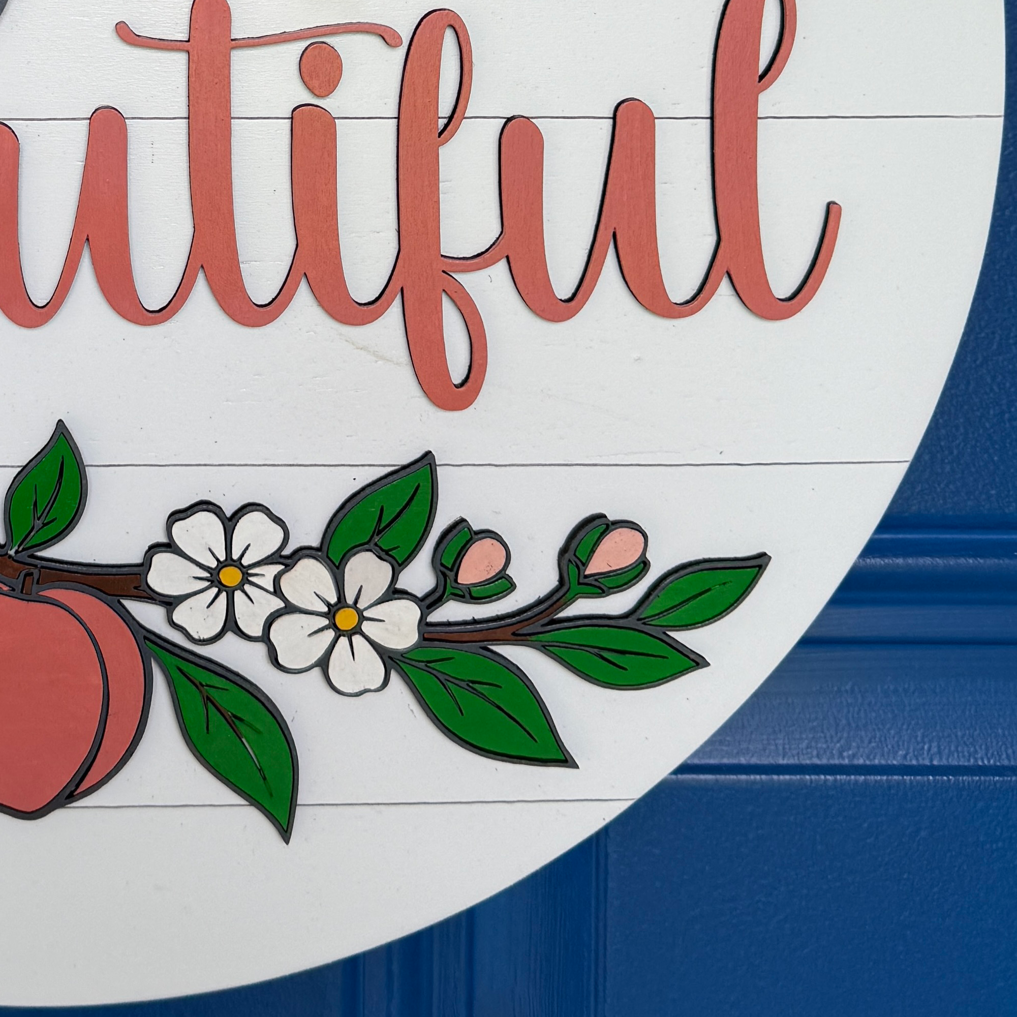 Detailed view of layered wood peaches, white blossoms, and greenery on a Hello Beautiful door hanger.
