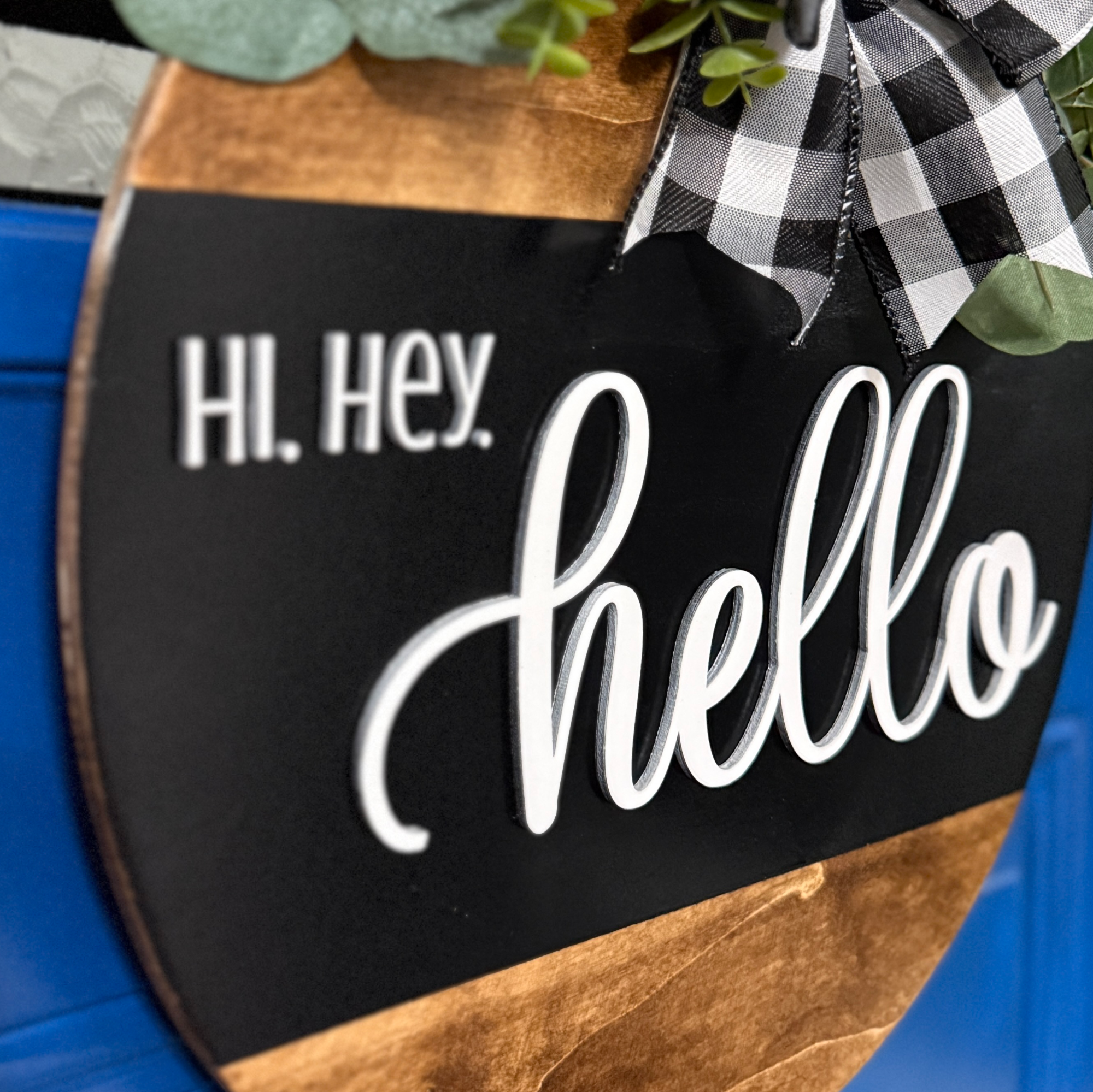 Side angle view of black hello door hanger with layered wood detail and buffalo plaid bow