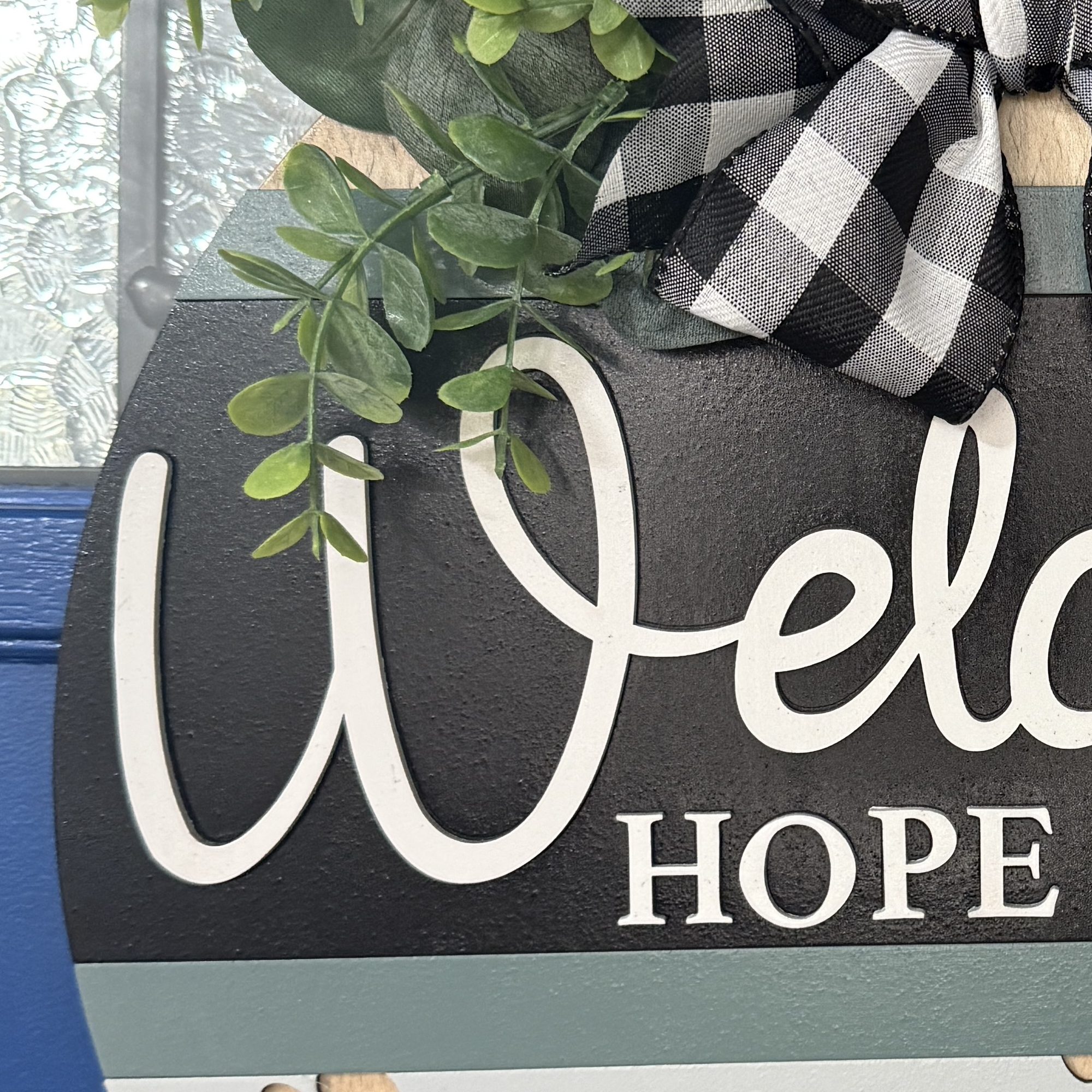Close-up of “Welcome Hope You Like Dogs” door hanger with paw prints, heart accent, and neutral colors, hanging on a blue front door.