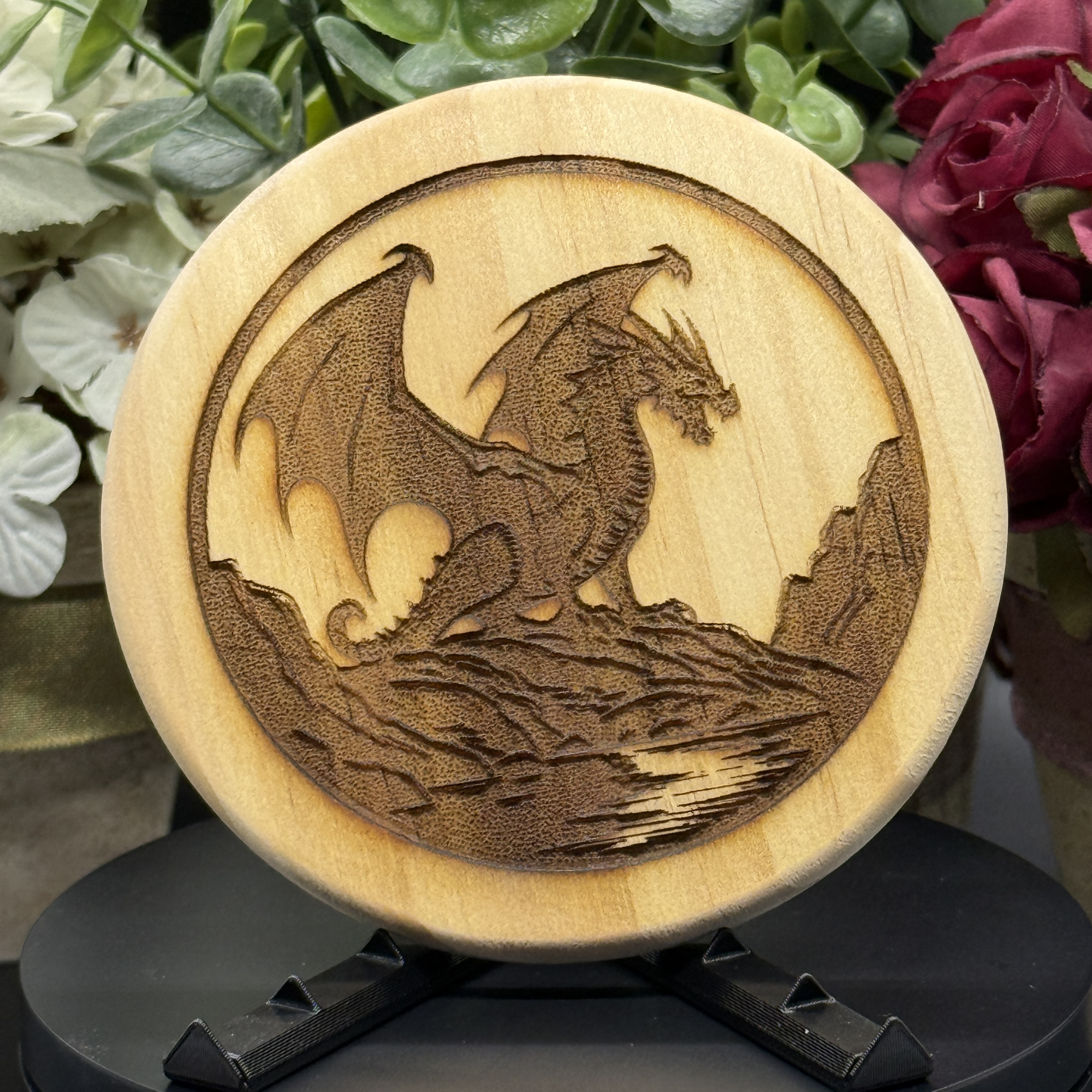 Round pine wood coaster with engraved dragon standing on a rocky cliff, wings spread wide in a dramatic silhouette