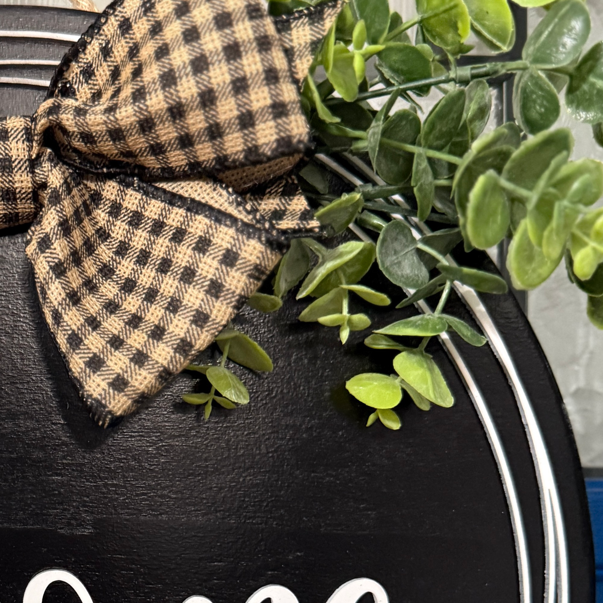 Detailed view of plaid ribbon bow and greenery accents on rustic black welcome door sign