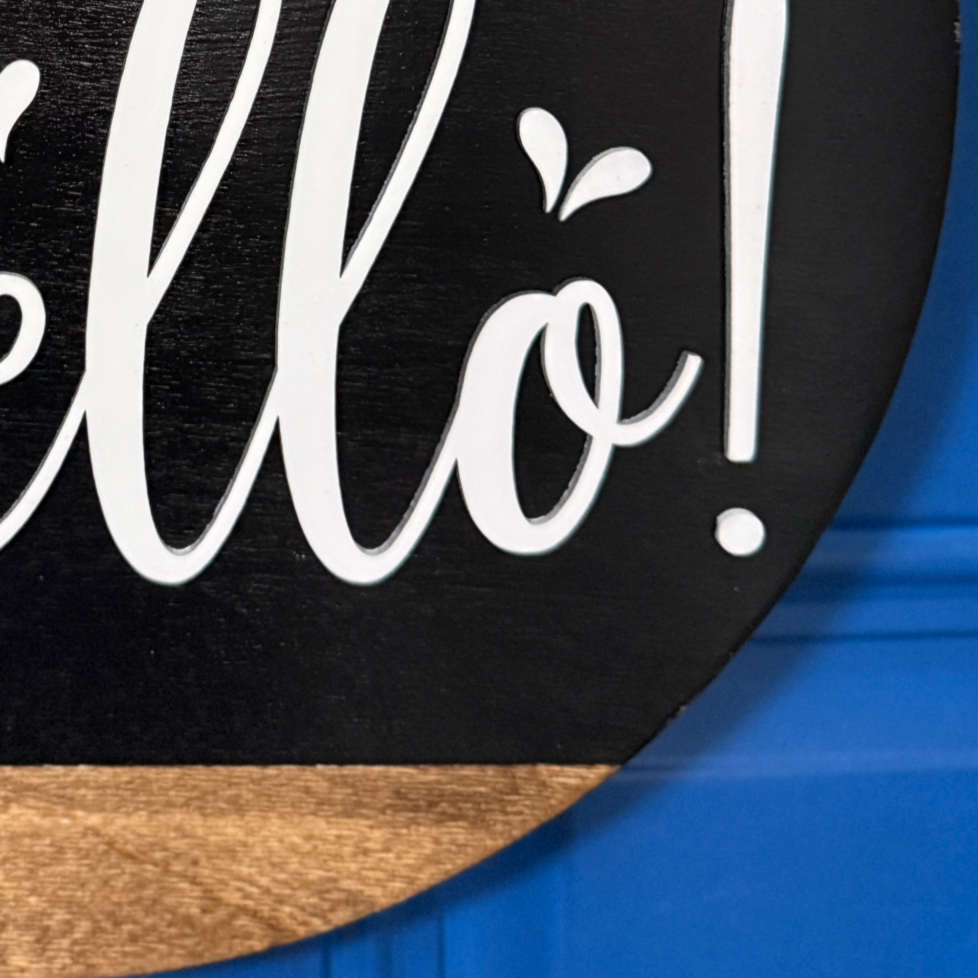 Close-up of white Hello script lettering on black painted wood door hanger with natural wood accent