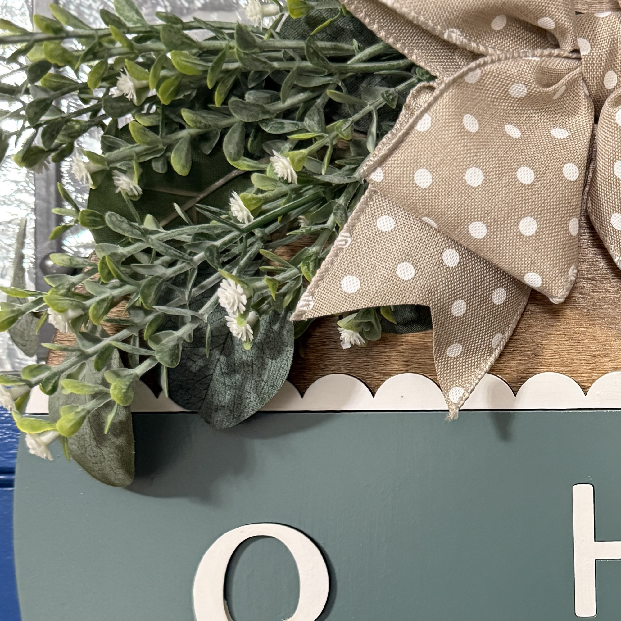 Close-up of greenery arrangement and neutral polka dot bow on top of patina blue Hello Spring door hanger