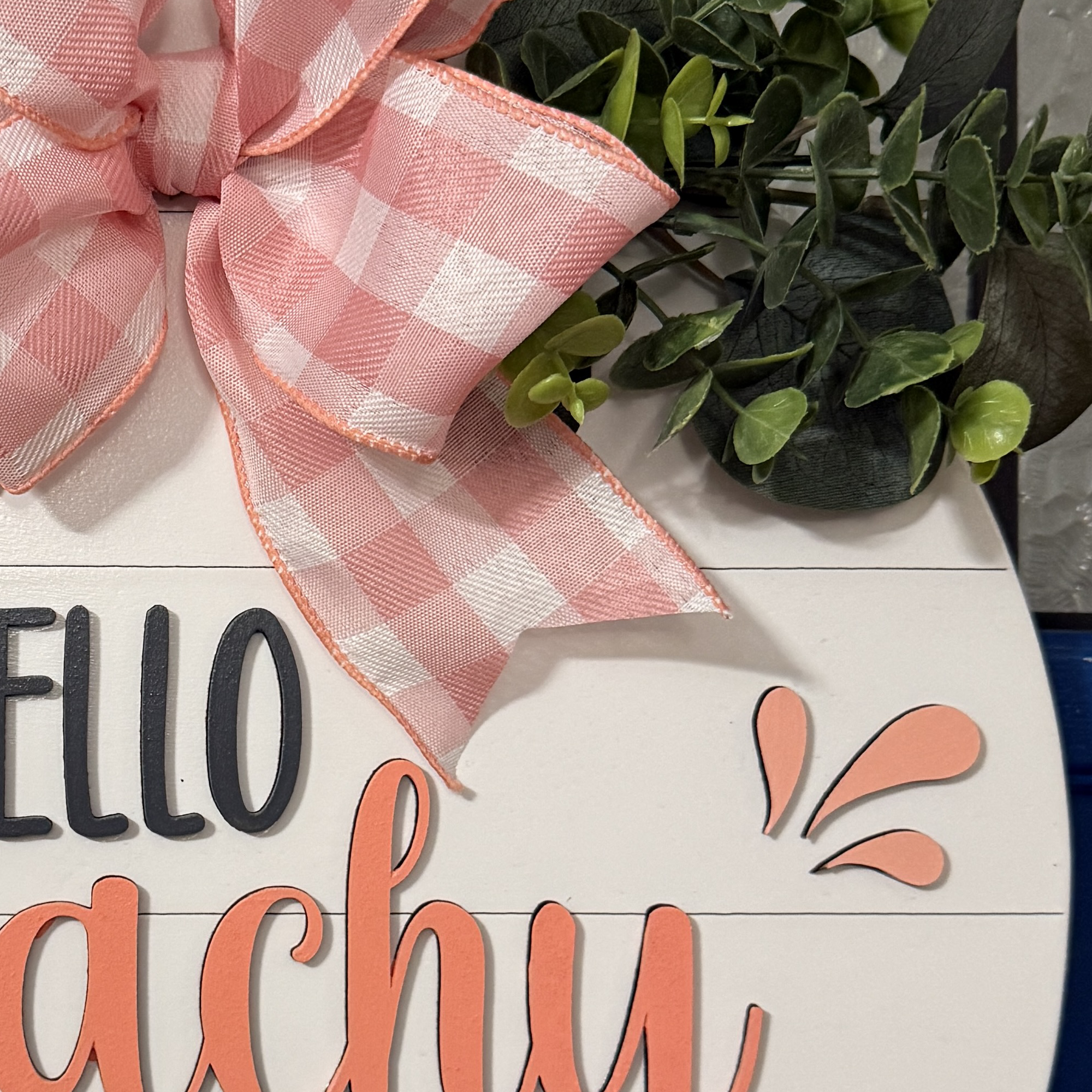 Close-up of raised peach-colored “Peachy” script lettering on white shiplap-style background
