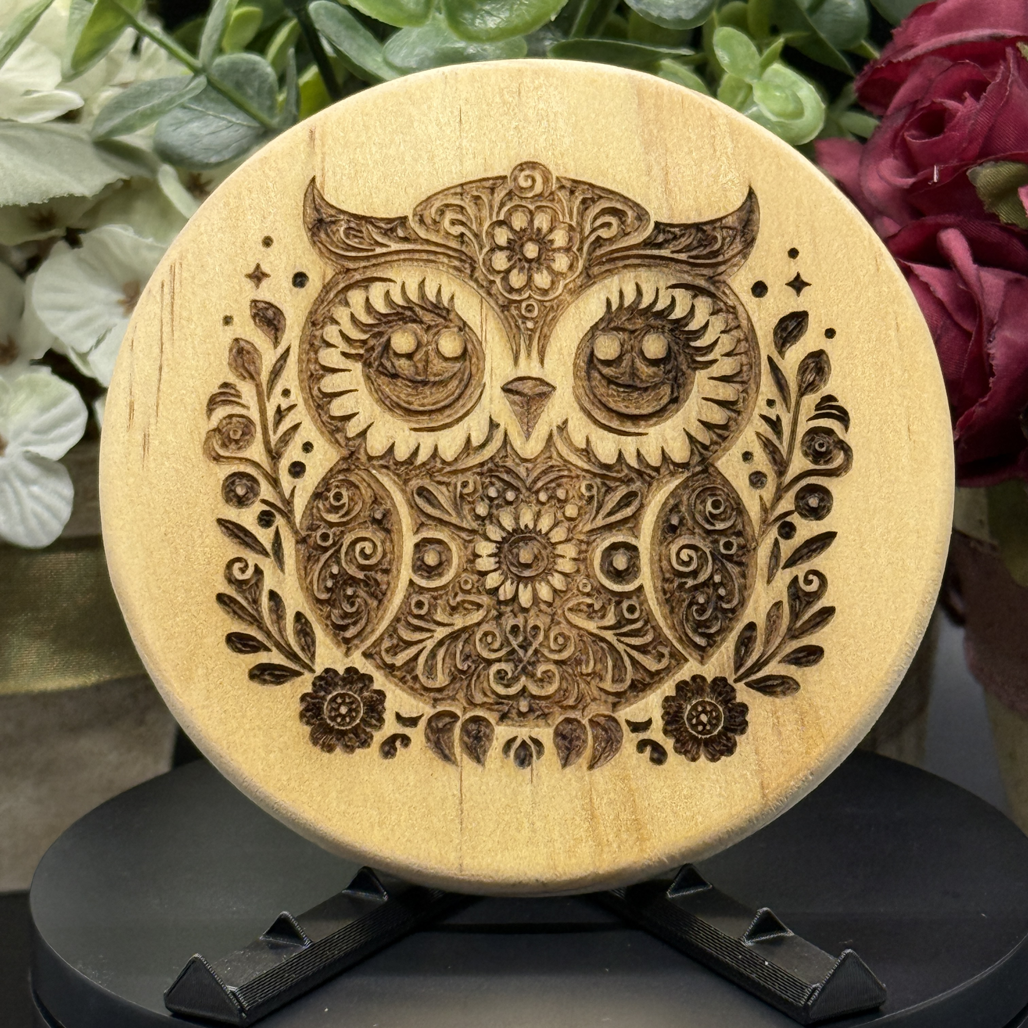 Round pine wood coaster with laser-engraved floral owl design, filled with ornate detailing and leafy accents