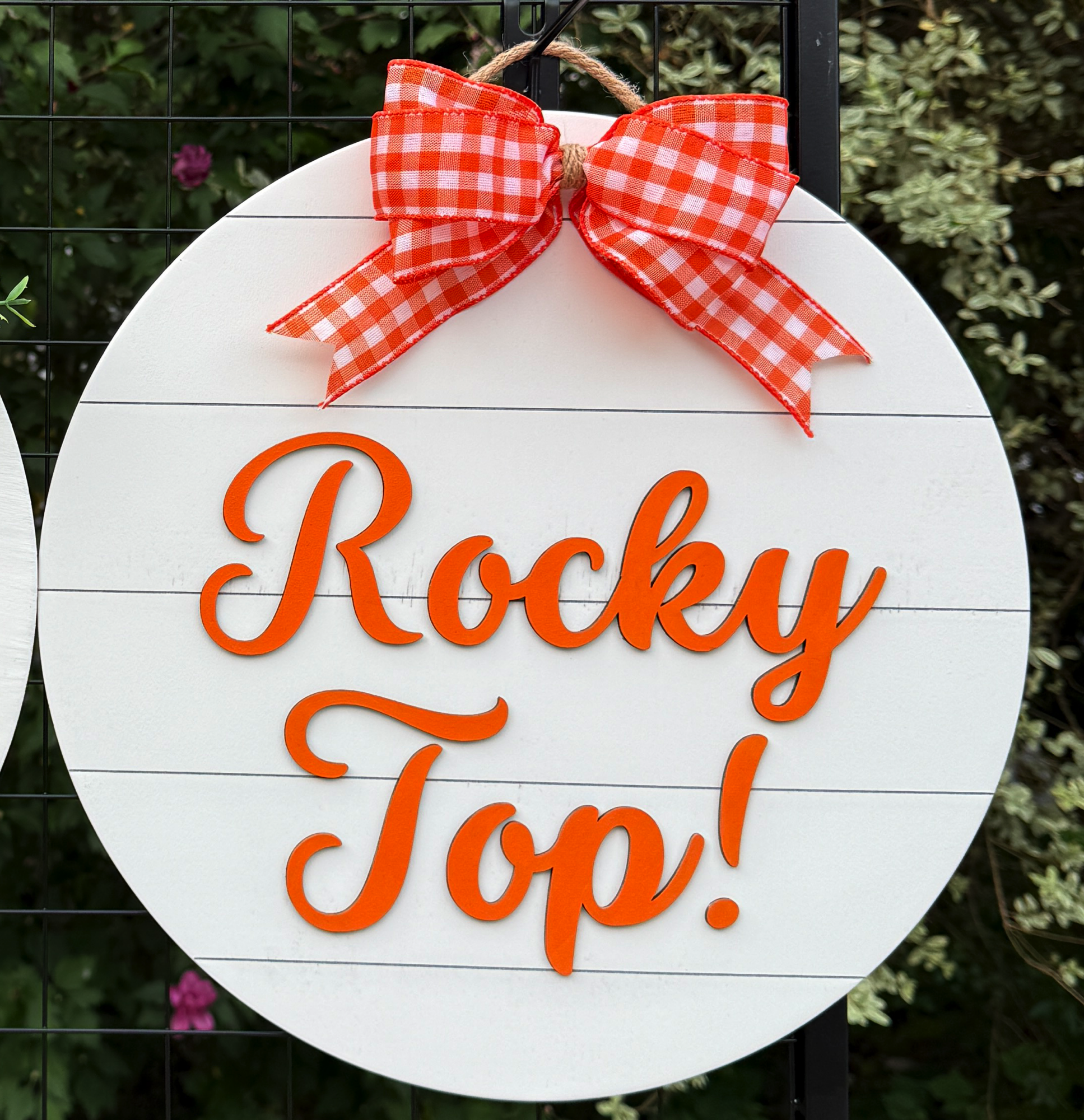 Round Rocky Top door hanger with orange script on white shiplap background and orange gingham bow
