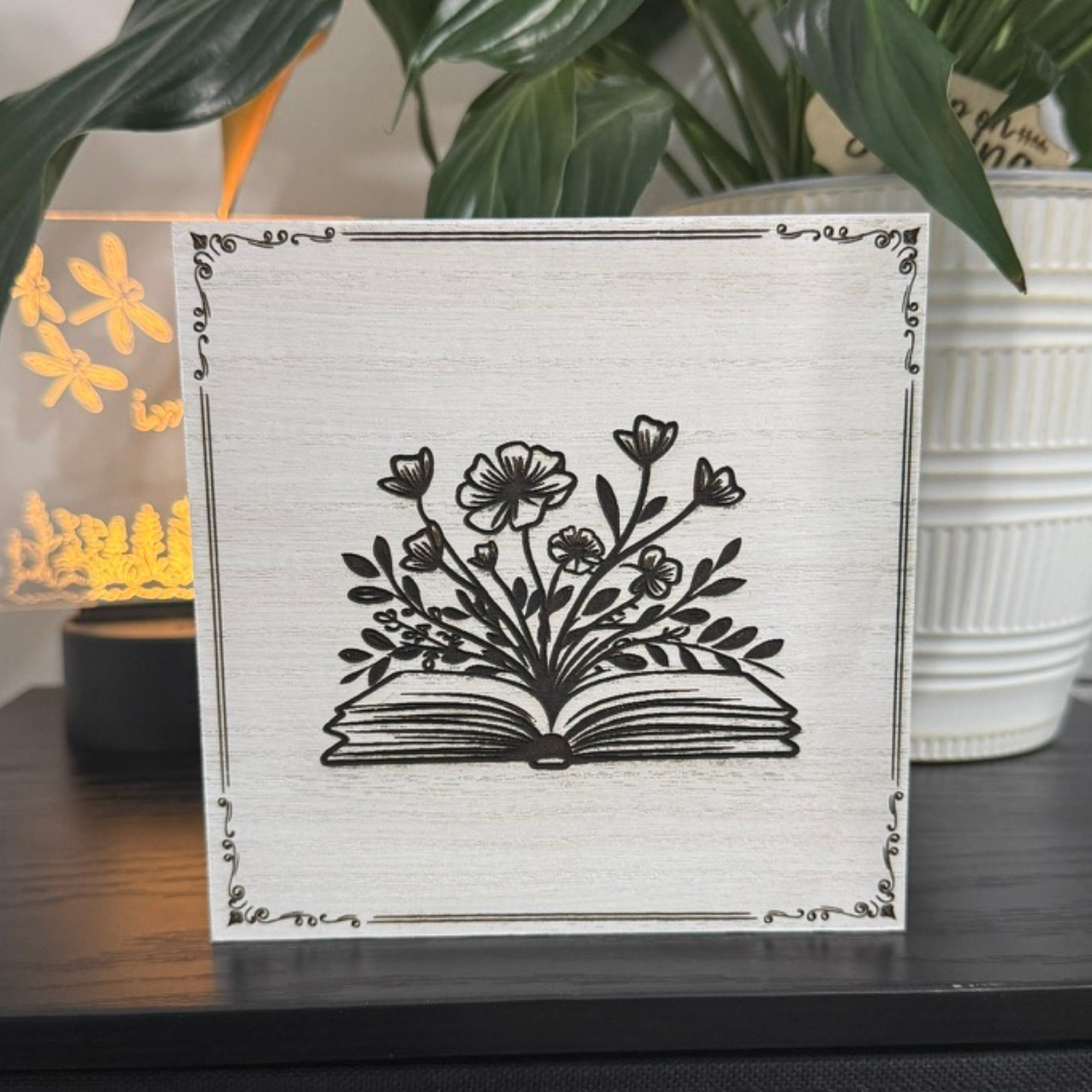 Close-up of fairy book shelf sitter featuring an open book with flowers rising from the pages, laser-engraved on white-washed wood