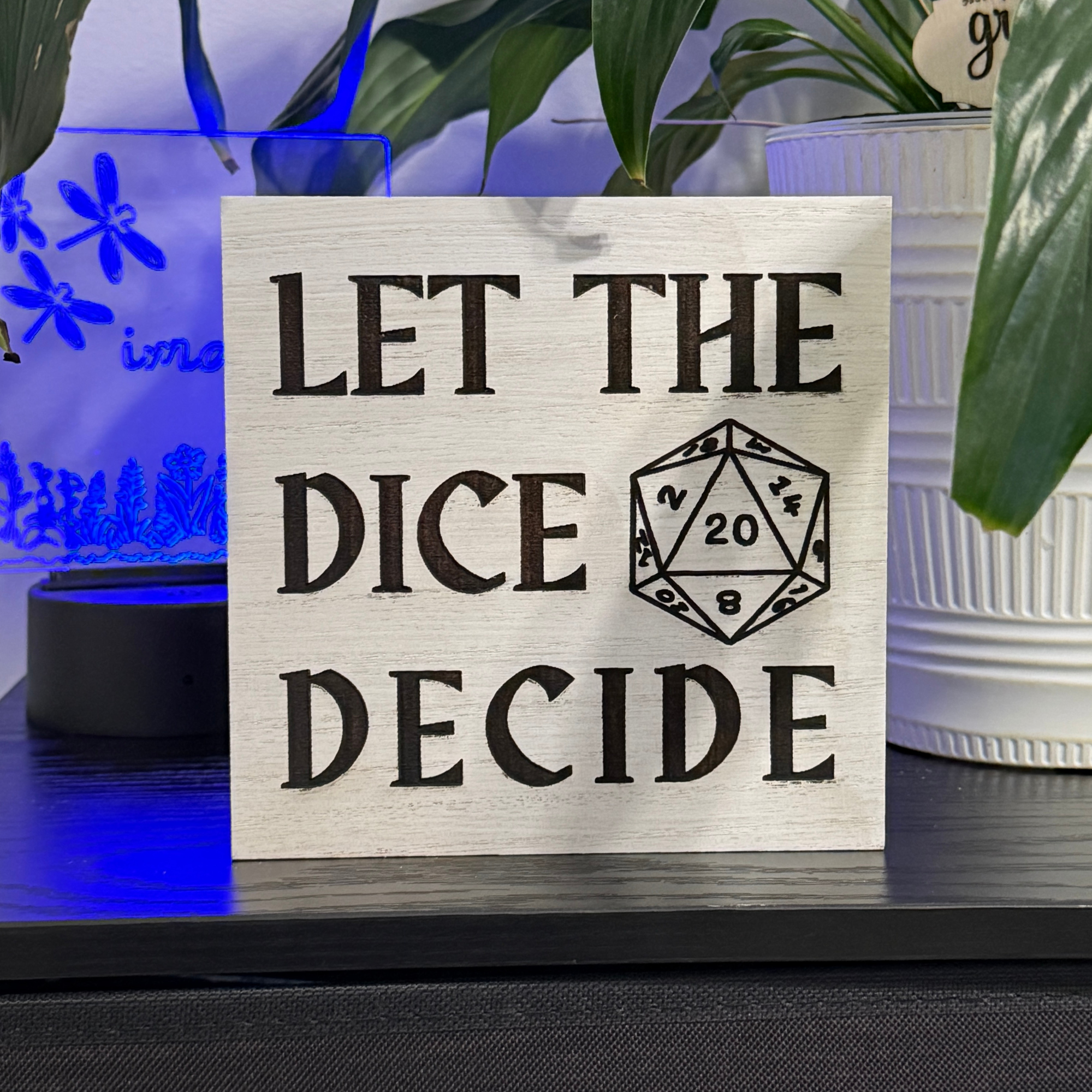 Wooden tabletop sign reading let the dice decide with d20 icon displayed with soft blue accent lighting