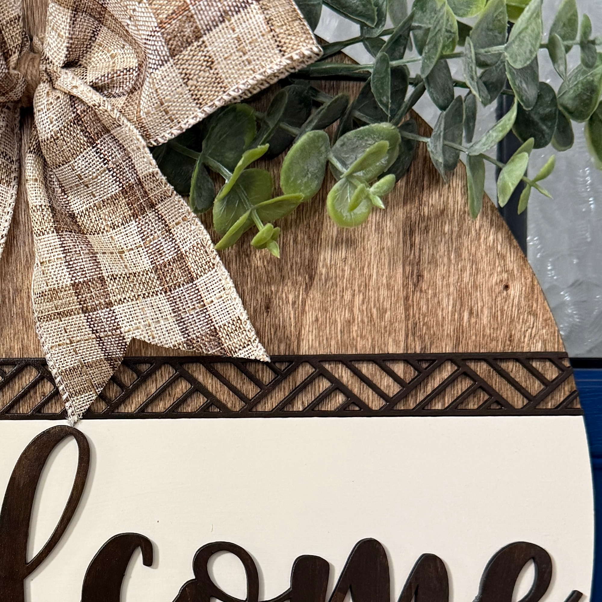 Close-up of greenery and plaid bow at top of rustic wood door hanger