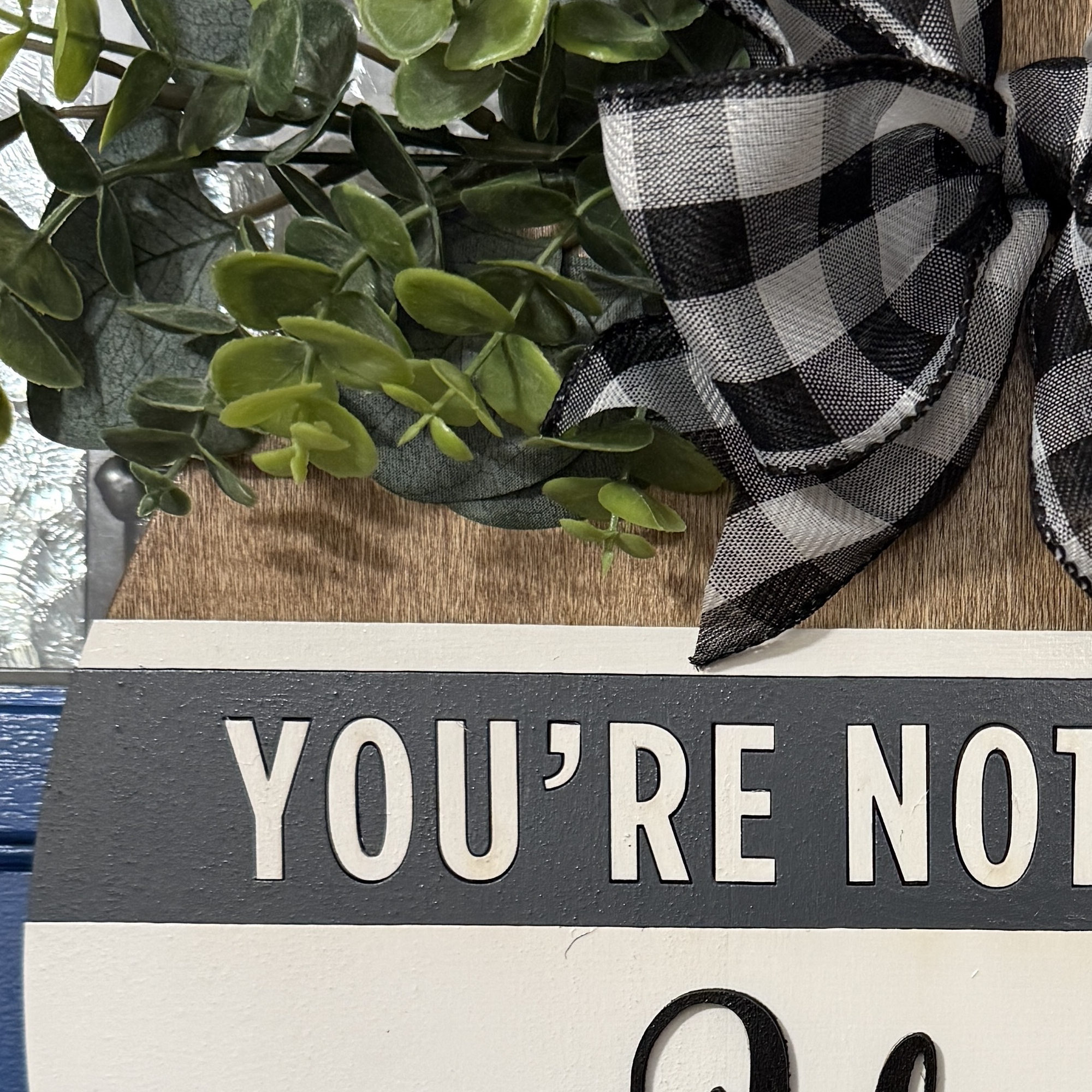 Close-up of gray header panel reading “You’re Not Welcome” with layered white lettering and buffalo plaid bow above.