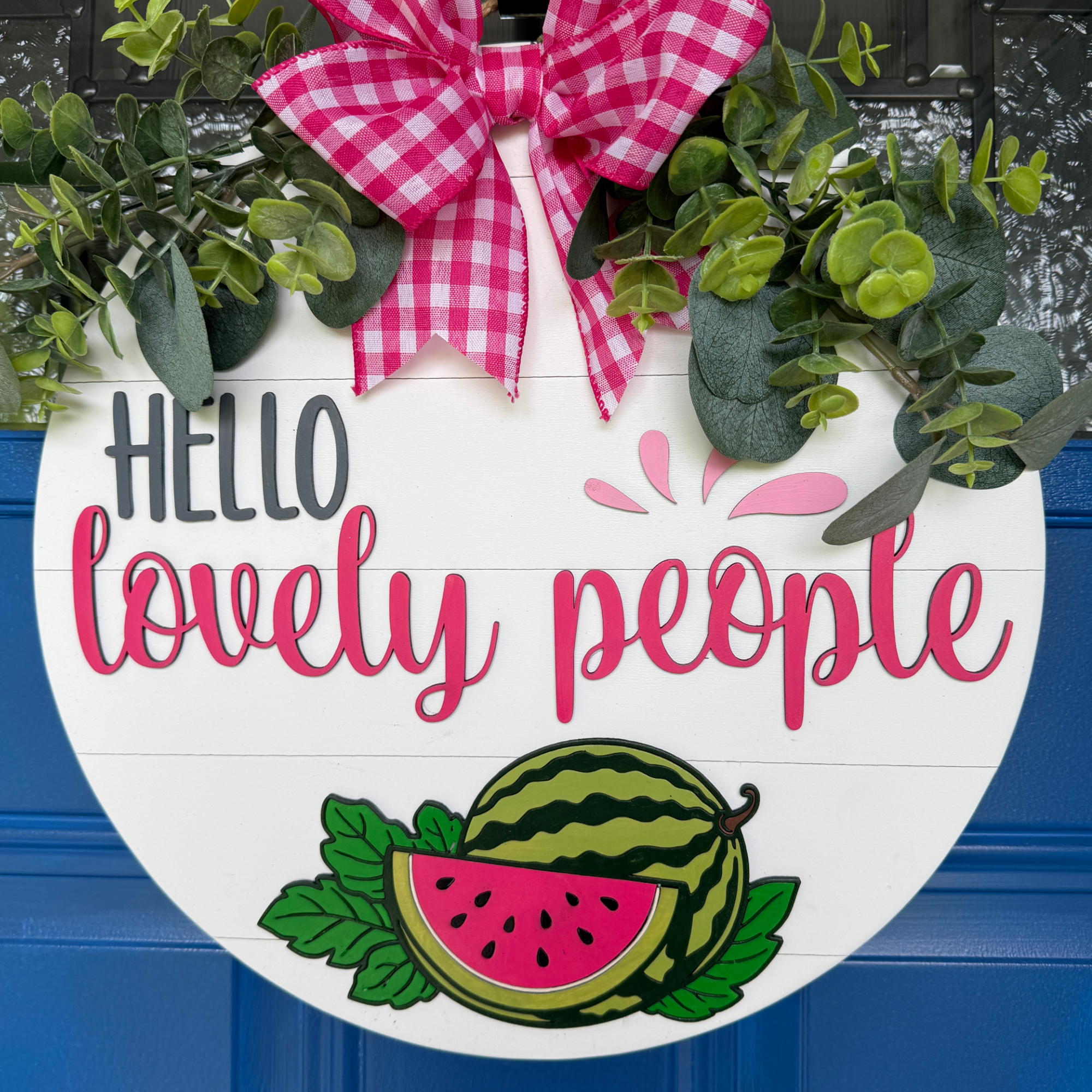 Handmade watermelon door hanger with Hello Lovely People lettering, pink gingham bow, greenery, and layered wood watermelon on white shiplap background.