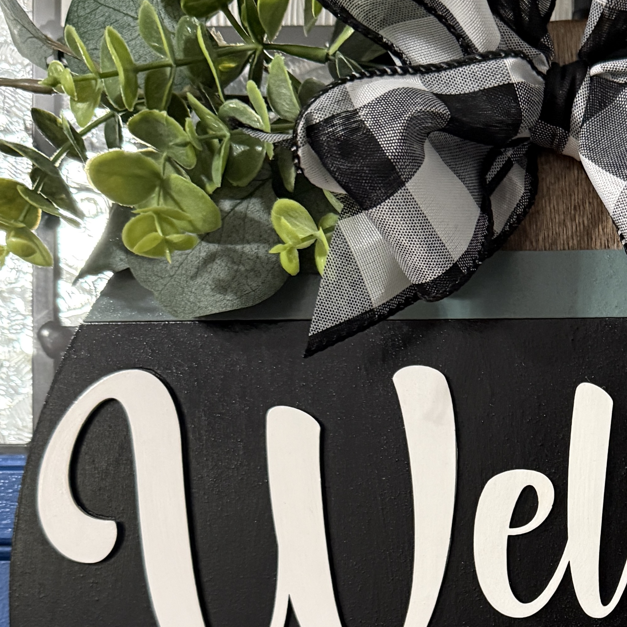 Close-up of greenery and black and white plaid bow at top of dog-themed door hanger