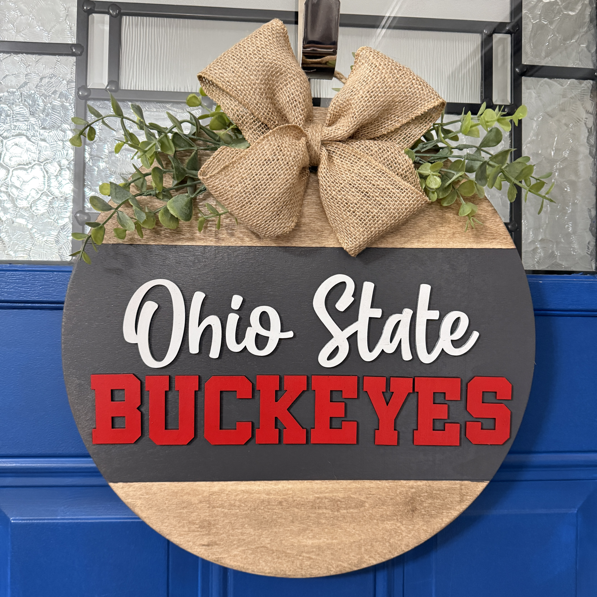 Front view of handcrafted Ohio State Buckeyes door hanger with red and gray design, burlap bow, and greenery