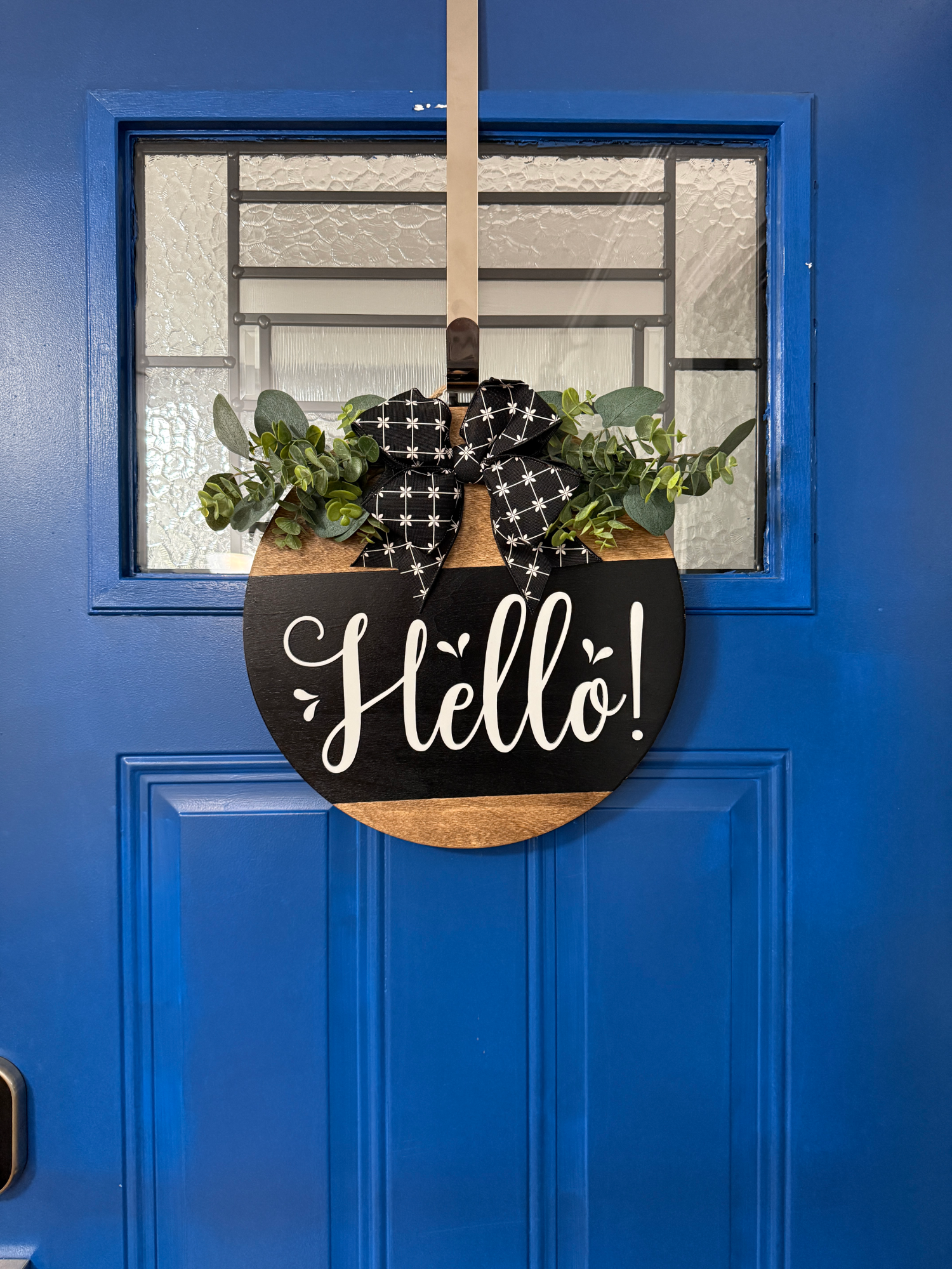 Full front door display featuring black and natural wood Hello door hanger with greenery and patterned bow