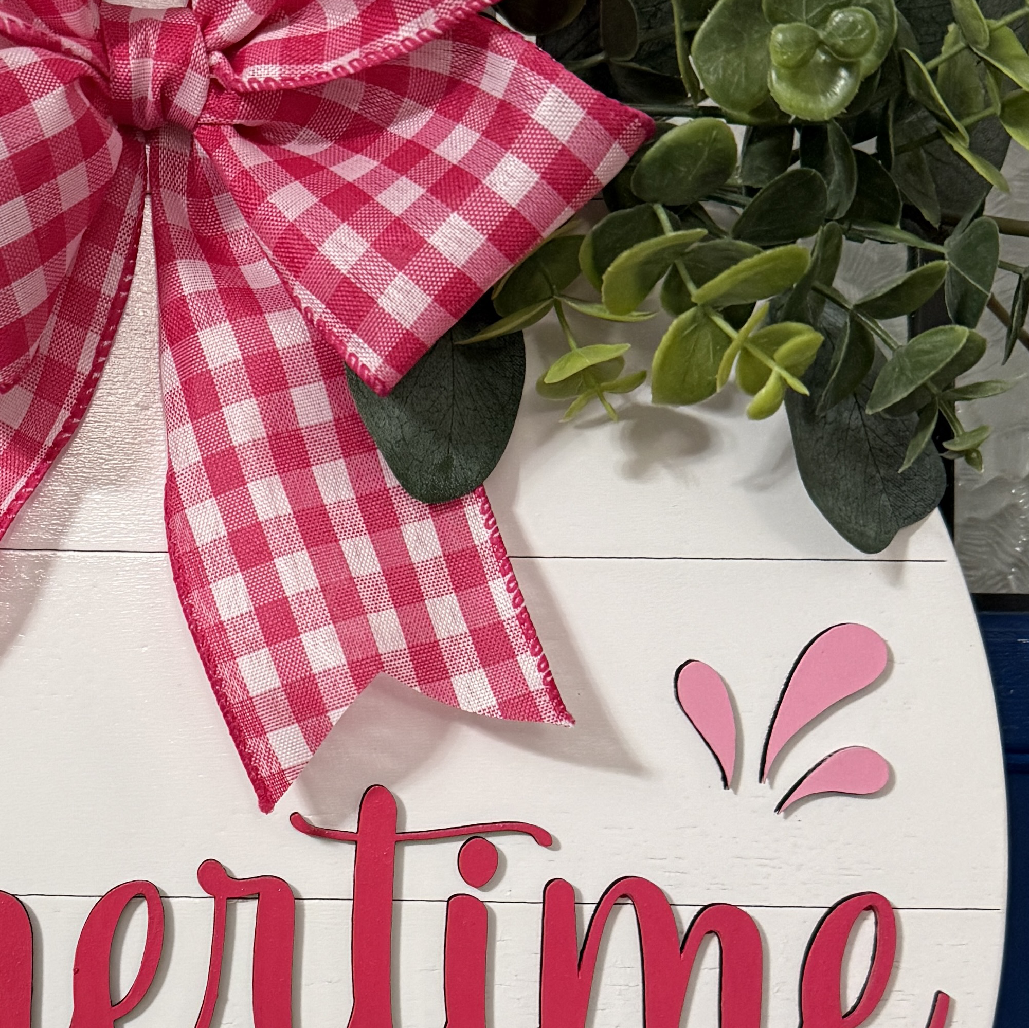 Detailed view of red gingham bow and layered greenery on top of summer front door decor
