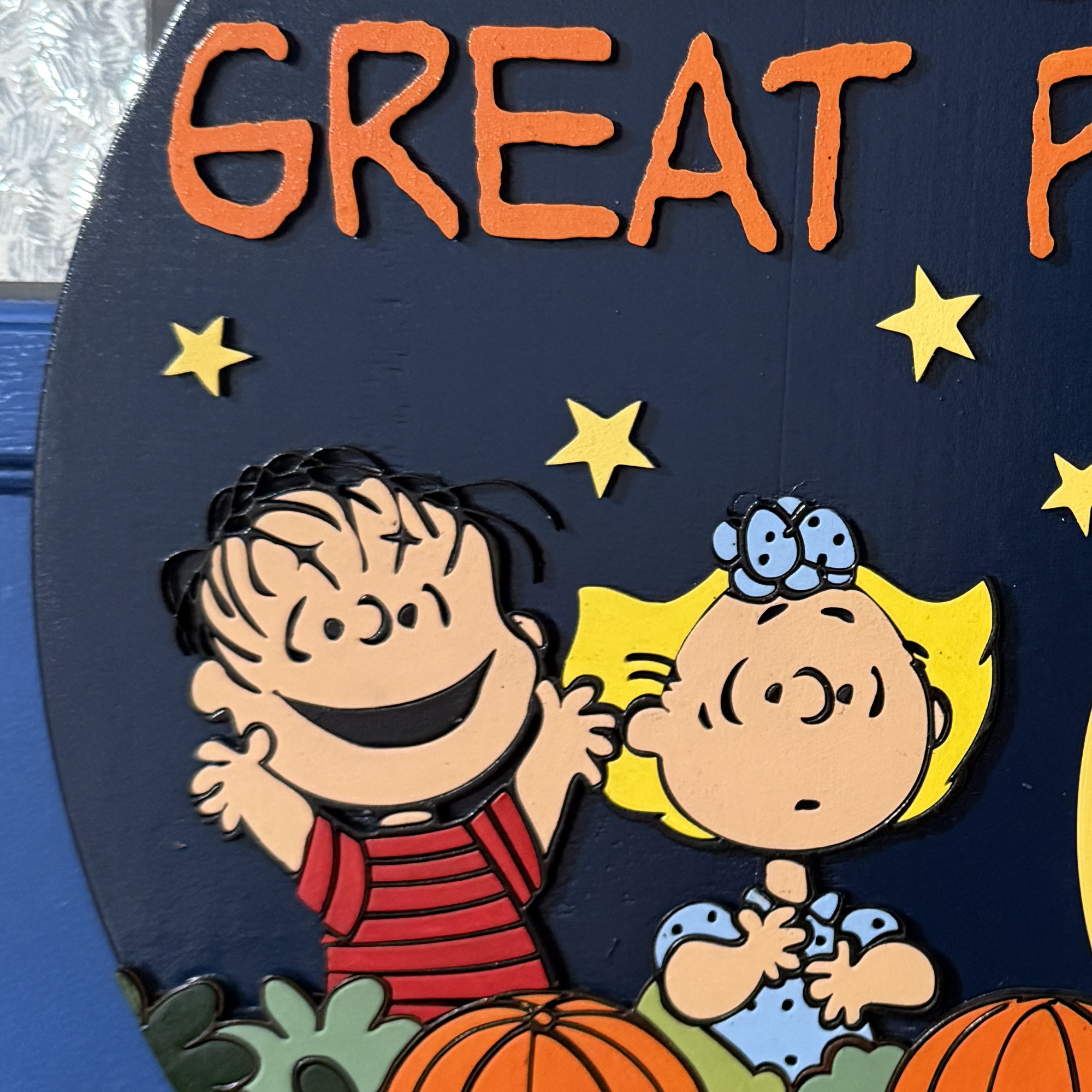Close-up of Peanuts characters Linus and Sally among pumpkins with stars and Snoopy’s moonlit silhouette