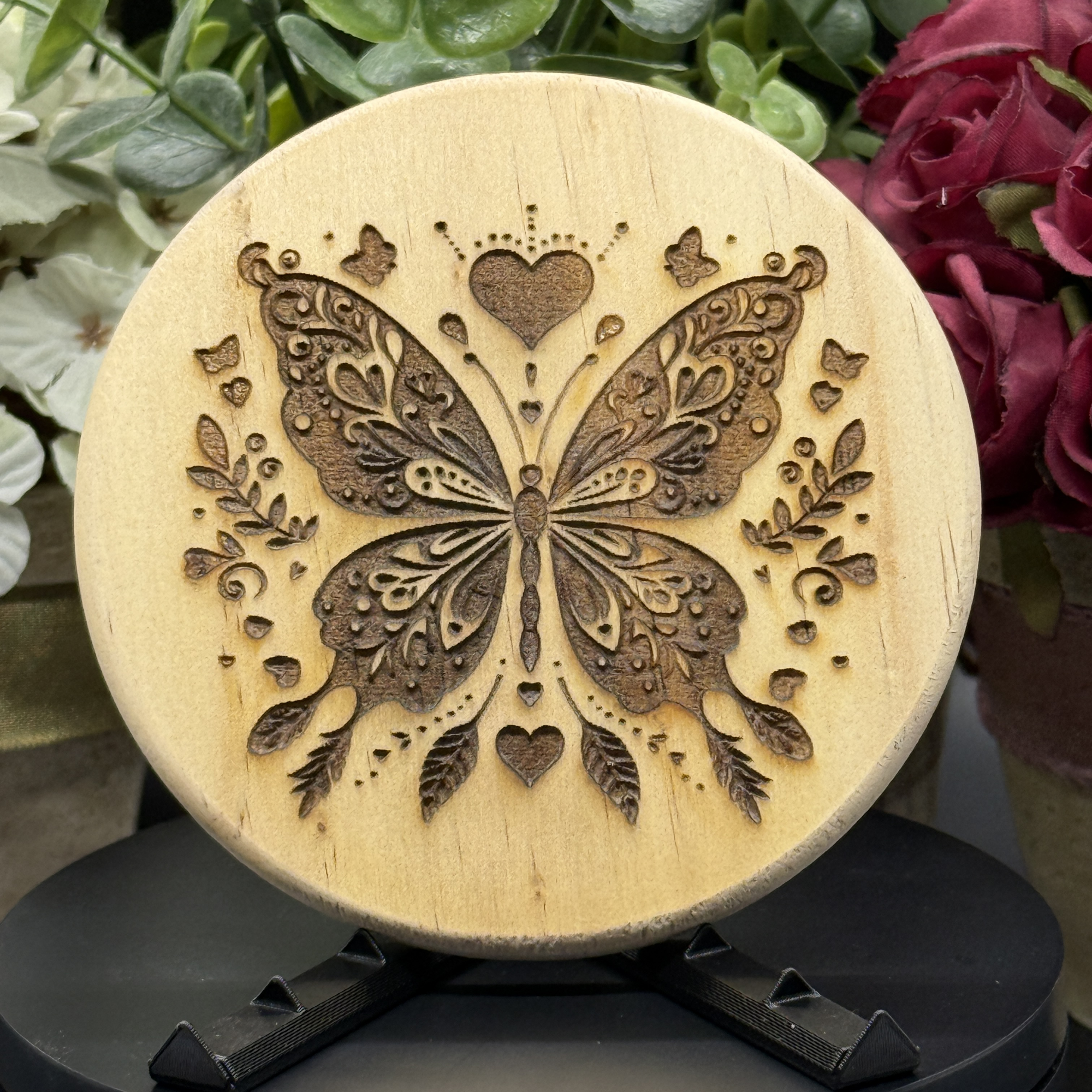 Round pine wood coaster with detailed butterfly and heart crown engraving, surrounded by leaves and mini butterflies