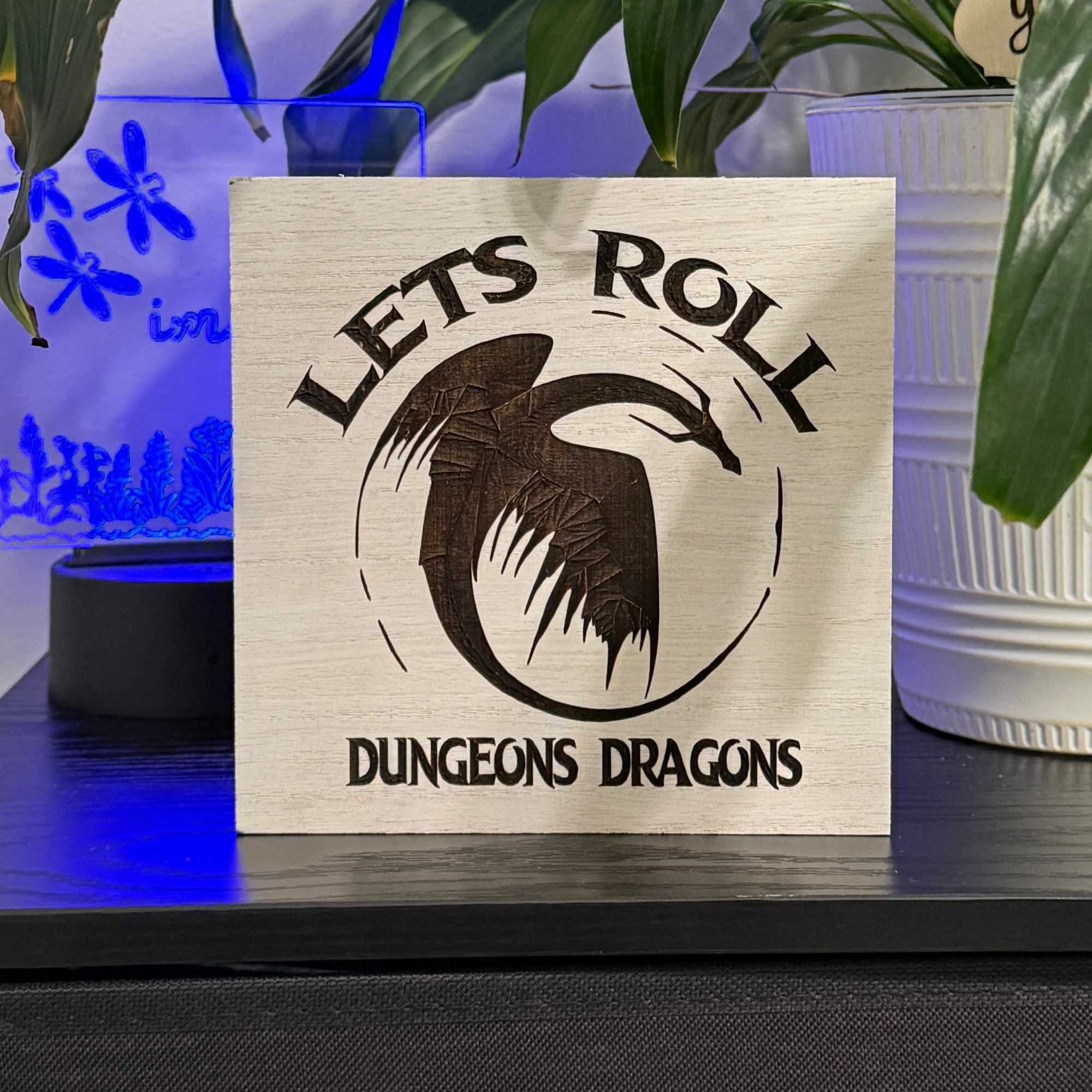 Wooden tabletop sign reading lets roll dungeons dragons displayed on shelf with blue accent lighting