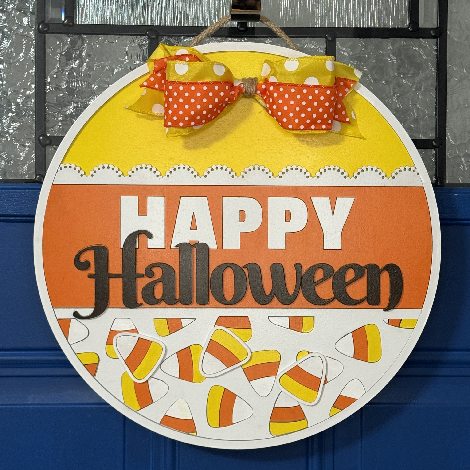 Front view of round Halloween door hanger with candy corn design, orange and yellow sections, “Happy Halloween” lettering, and polka-dot bow