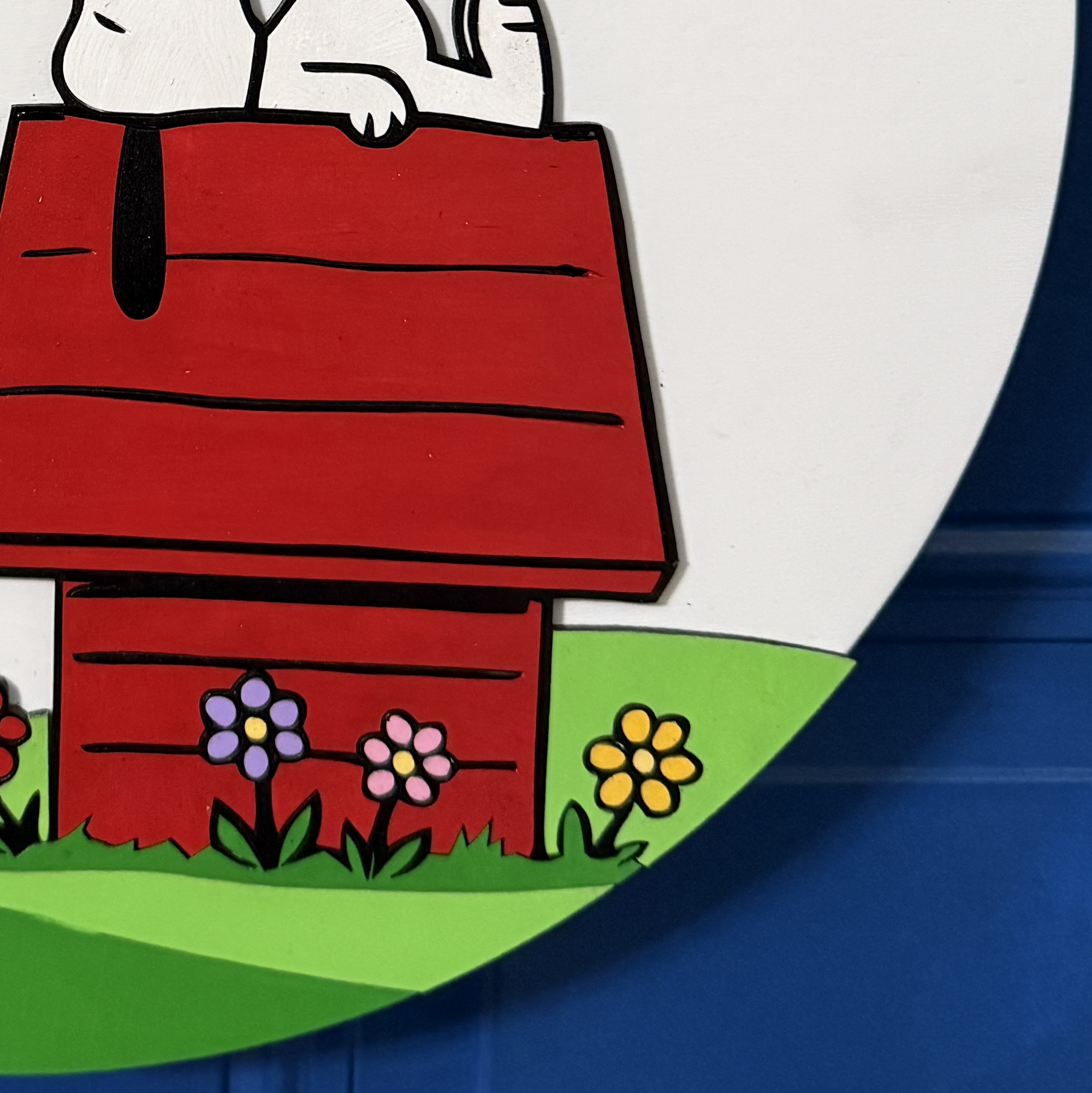 Close-up of red doghouse with flowers and green grass along bottom of sign