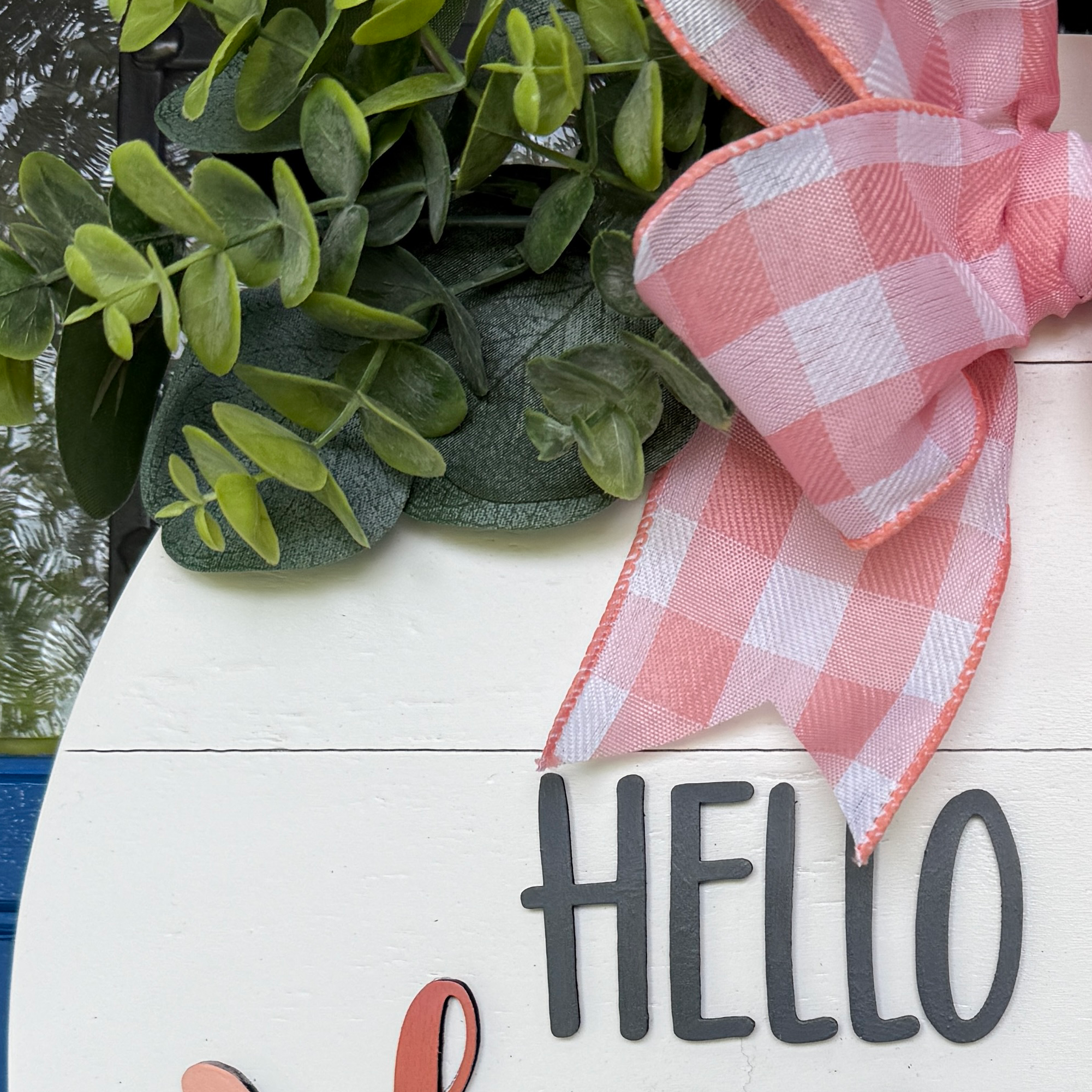 Close-up of pink gingham bow, eucalyptus greenery, and Hello lettering on a handmade peach door hanger.
