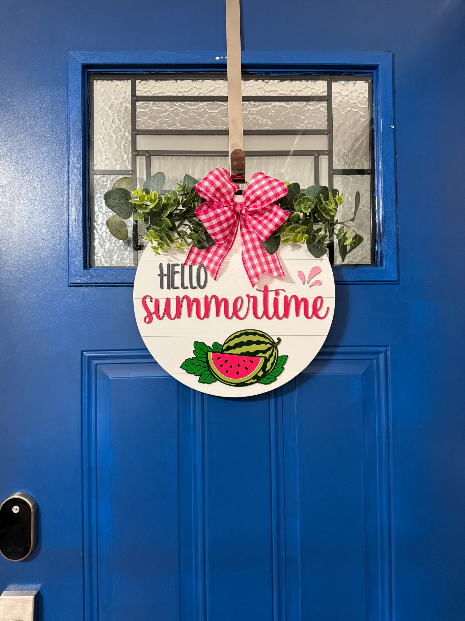 Full view of Hello Summertime watermelon door hanger displayed on bright blue front door with red gingham bow