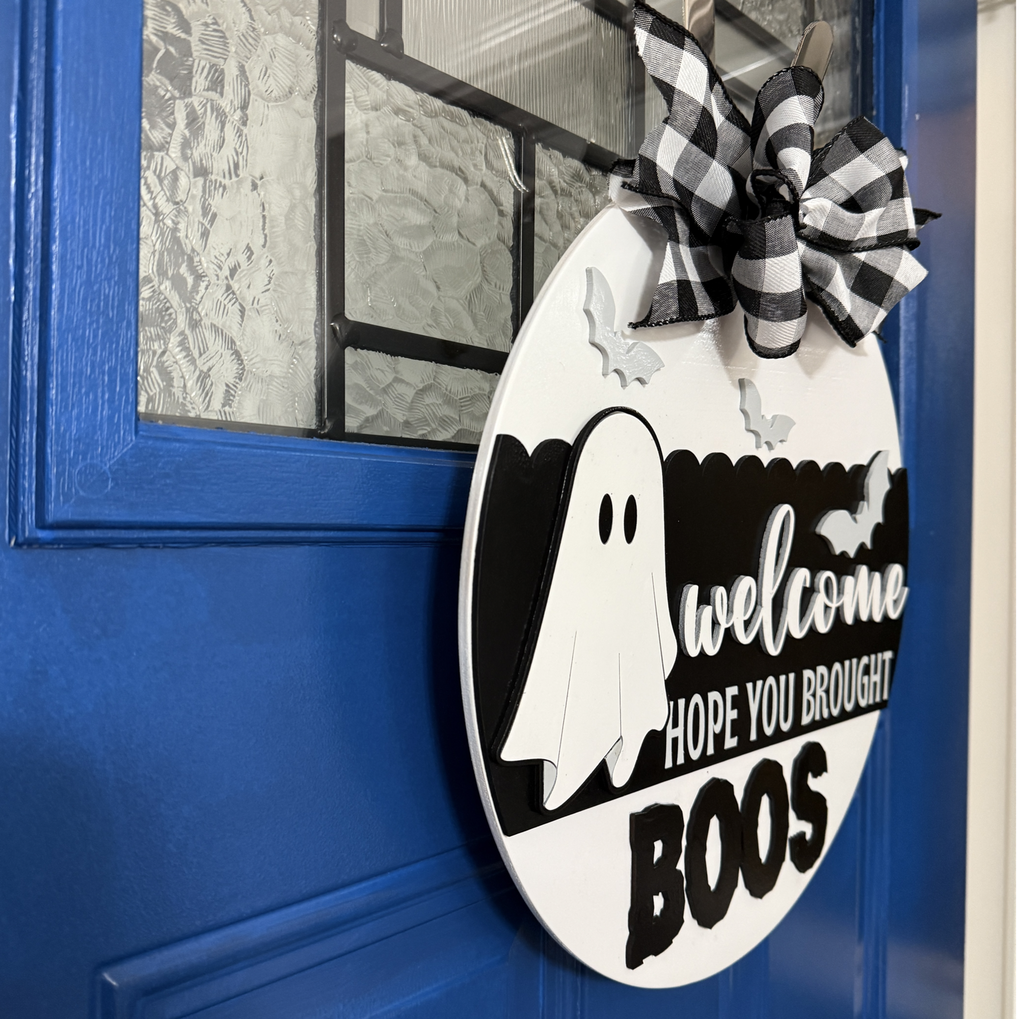 Side angle view of round wooden Halloween door hanger showing layered ghost and bats design with raised lettering