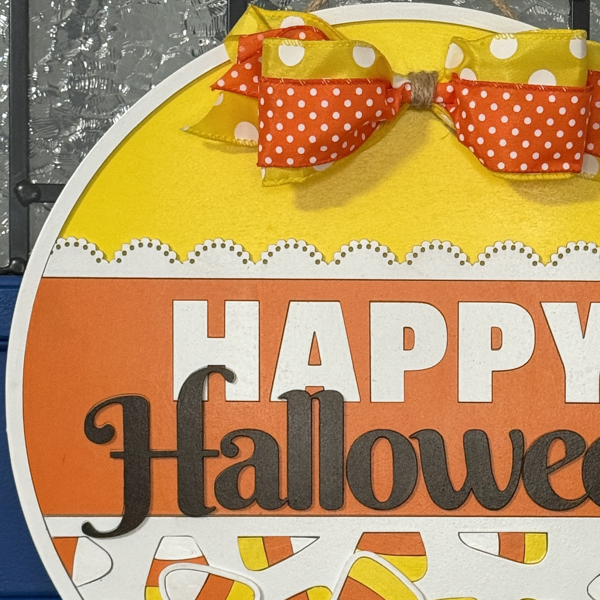 Close-up of Halloween candy corn door hanger with bow, hanging on a blue front door