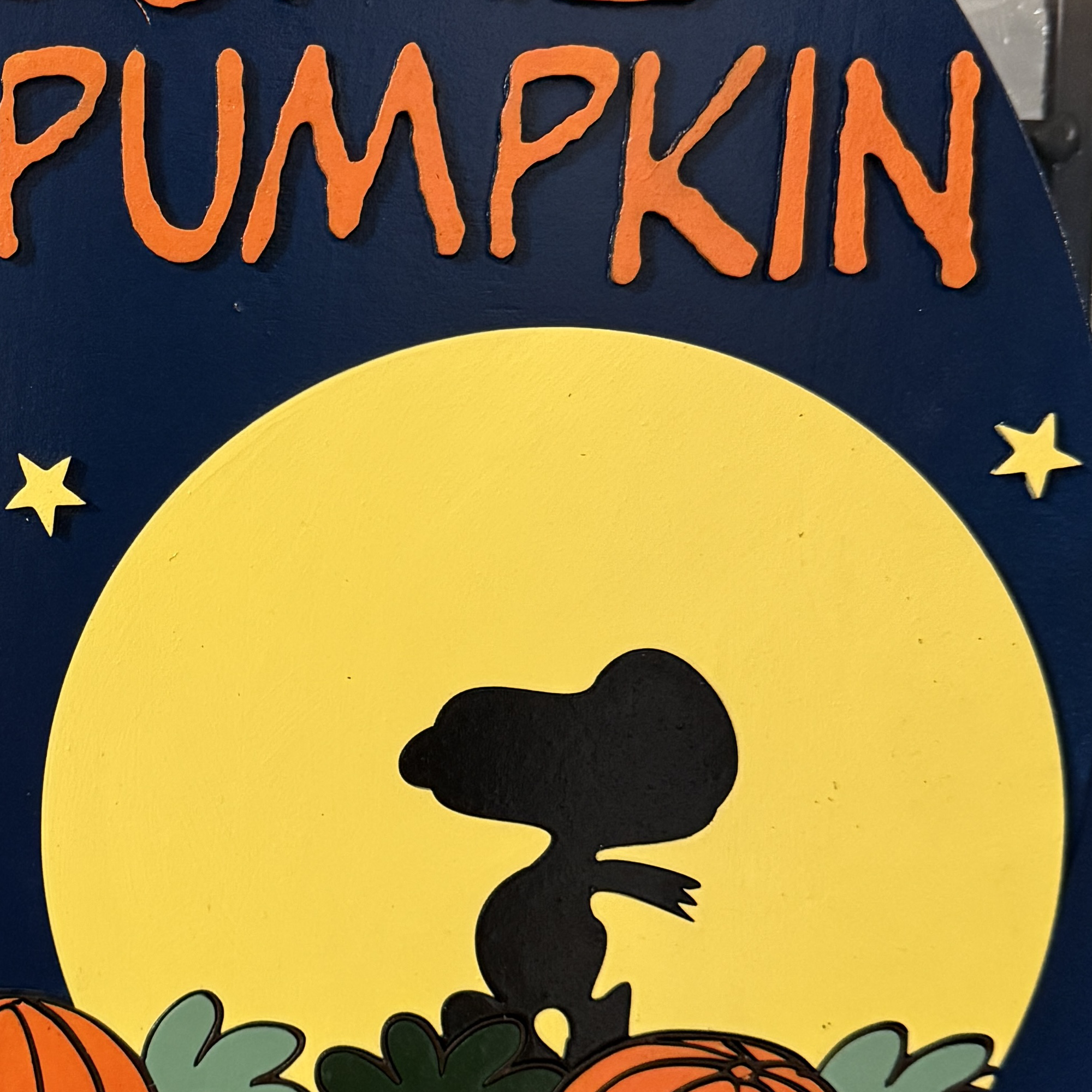 Close-up of Peanuts characters Linus and Sally among pumpkins with stars and Snoopy’s moonlit silhouette