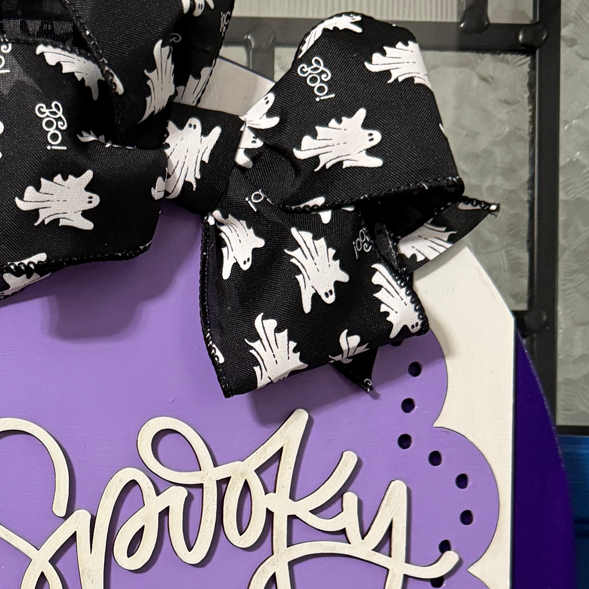 Close-up of black Halloween bow with white ghost and leaf pattern above layered Spooky and Sweet lettering