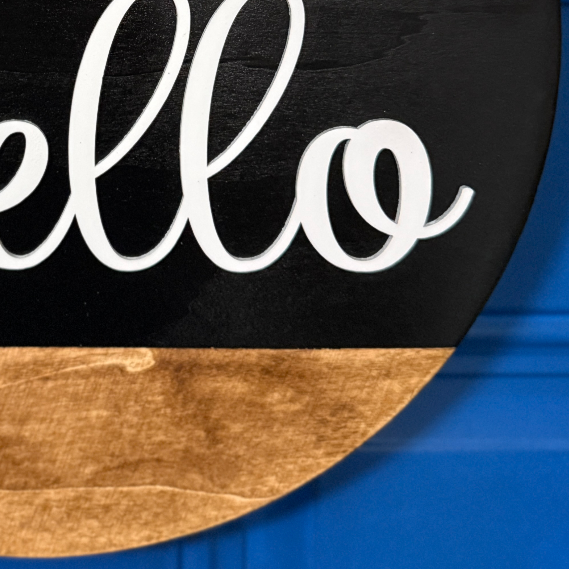 Close-up of white hello script lettering on black painted wood door hanger with natural stained wood accent