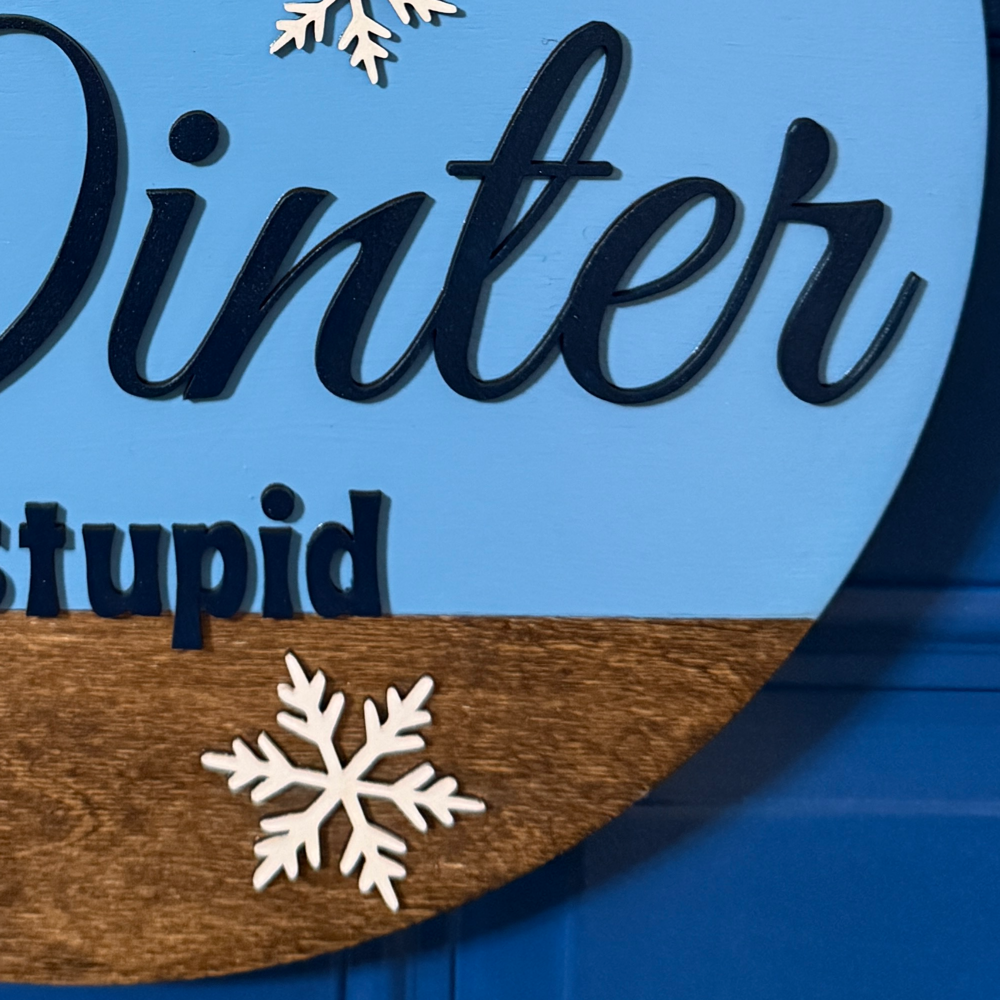 Close up of layered white snowflake accent on the lower portion of Winter Is Stupid wooden door hanger