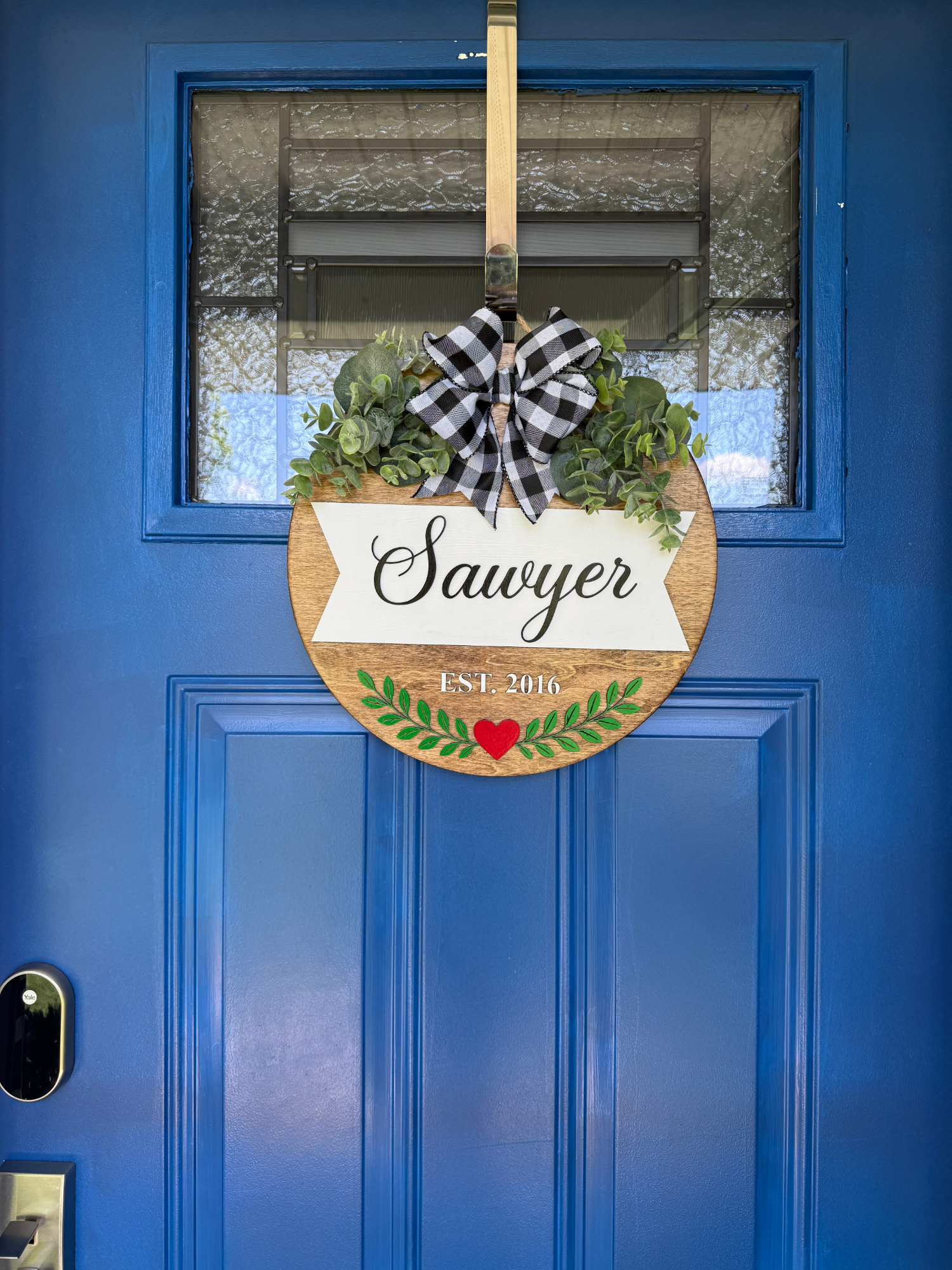 Handcrafted family name door hanger displayed on a blue front door.