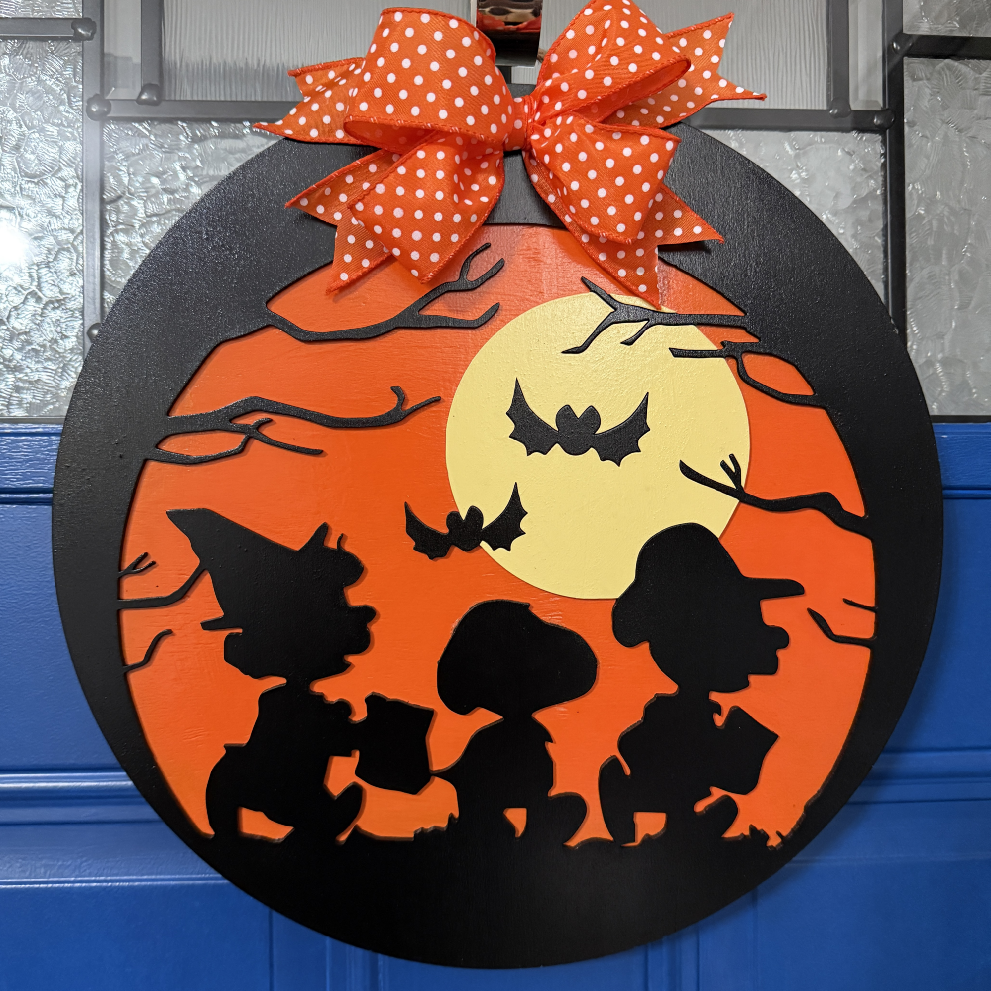 Front view of Trick-or-Treat Halloween door hanger with Peanuts silhouettes, glowing moon, bats, and orange bow