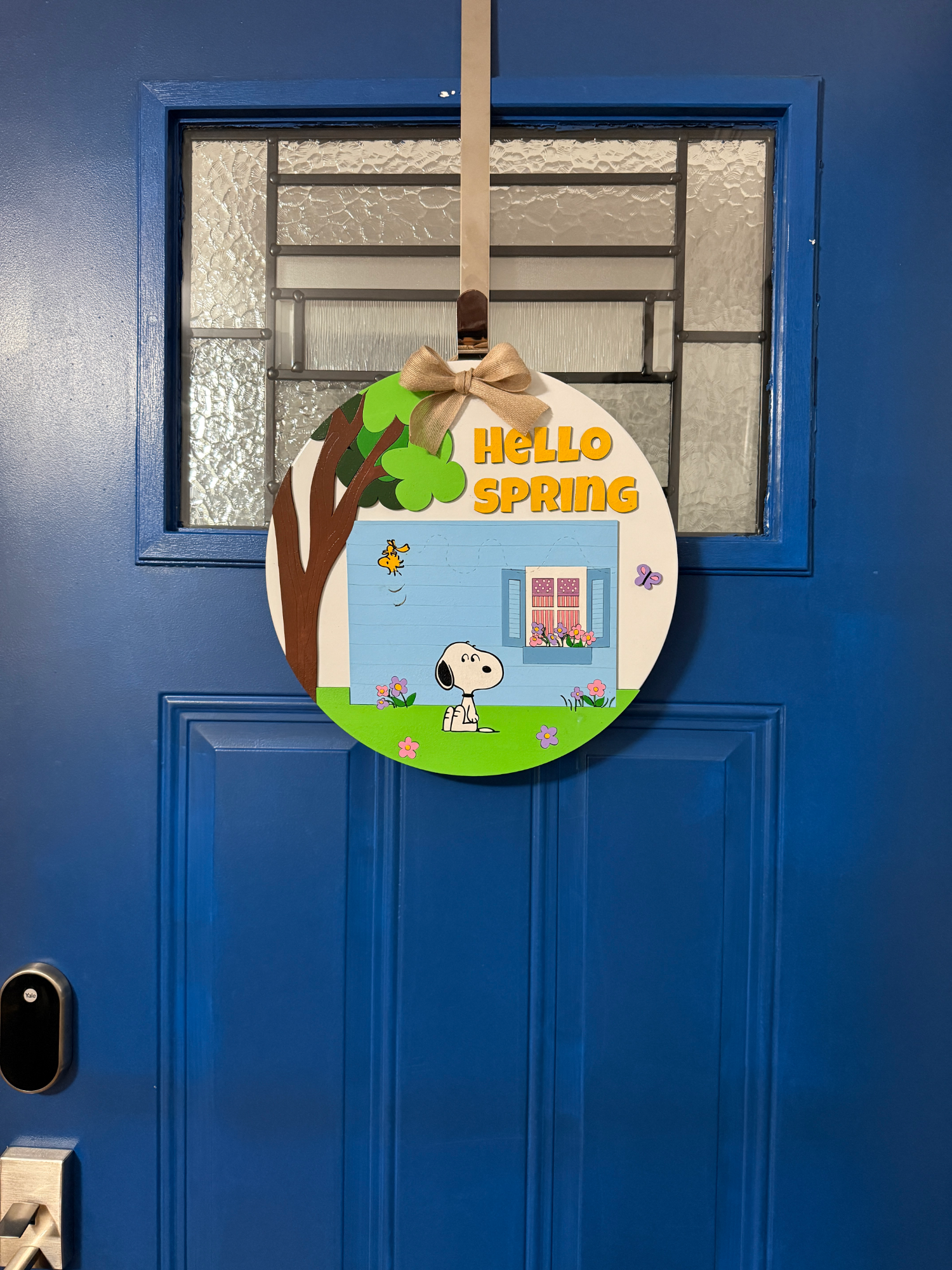 Full view of round spring door sign with tree, house, flowers, and “Hello Spring” text