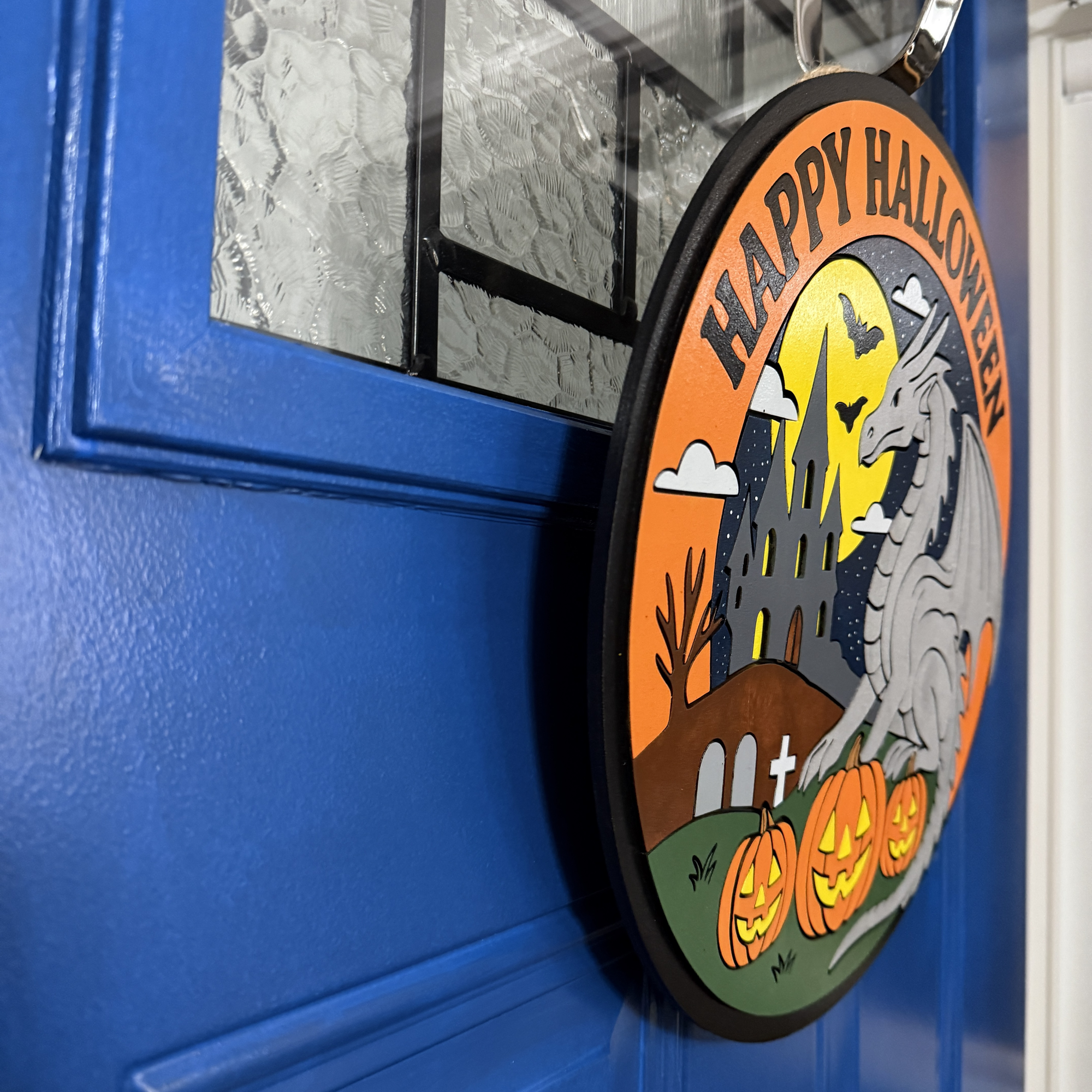 Side angle of round dragon Halloween door hanger showing layered wood design and jute rope hanger