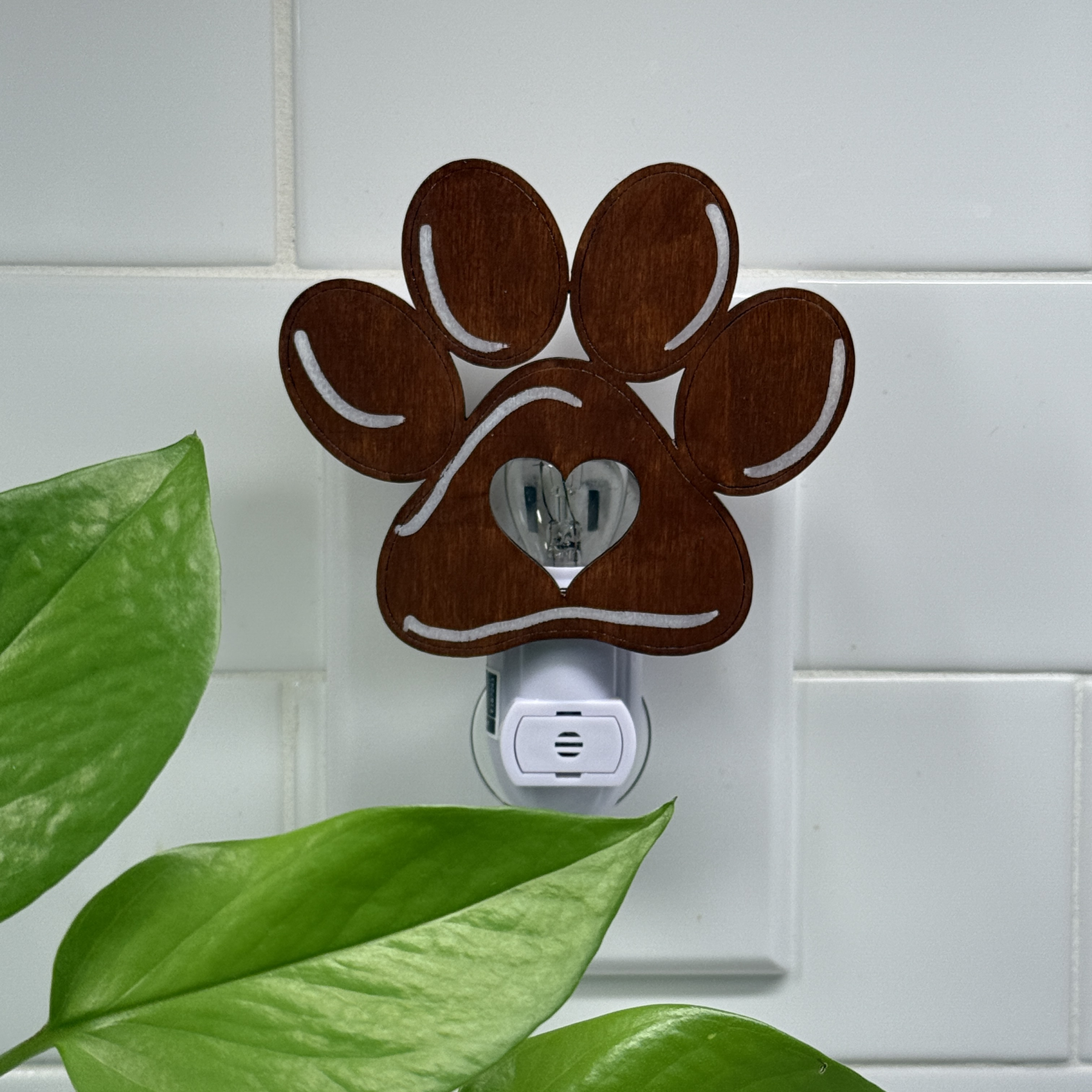 Brown paw print night light with heart cutout, shown in daylight on white tile backdrop
