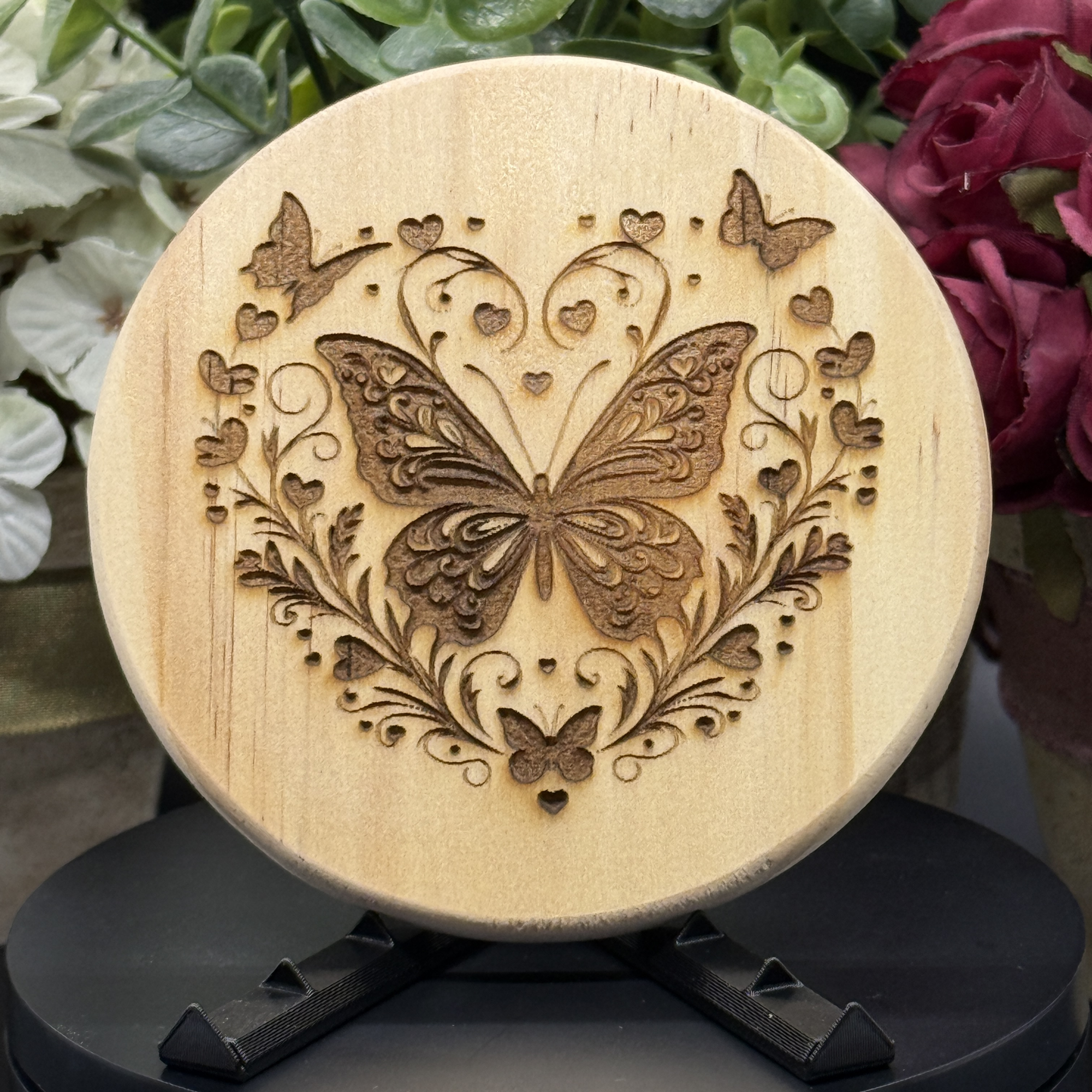 Round pine wood coaster with laser-engraved butterfly and heart flourish design, surrounded by floral elements