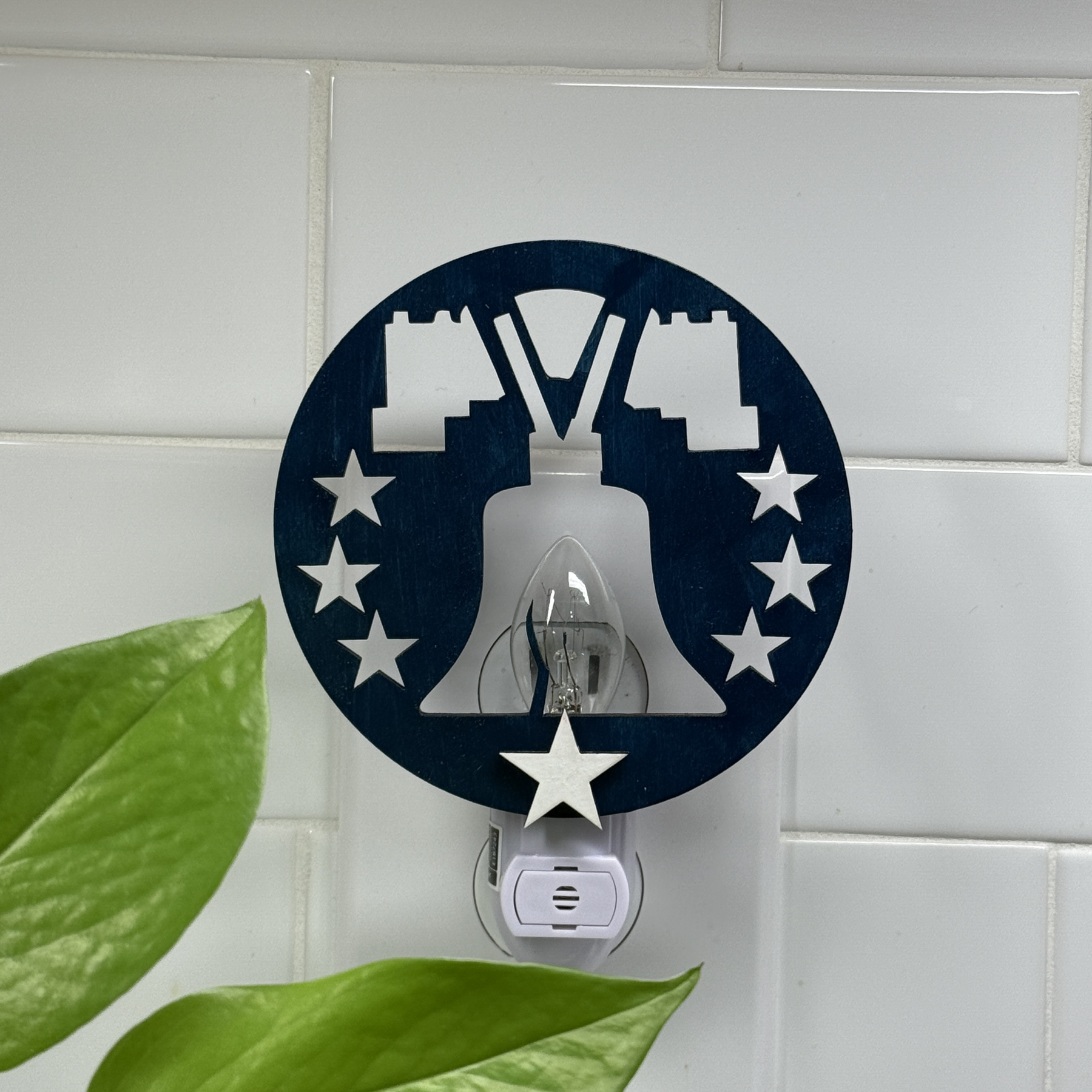 Patriotic Liberty Bell night light in navy and white, plugged into white tile wall