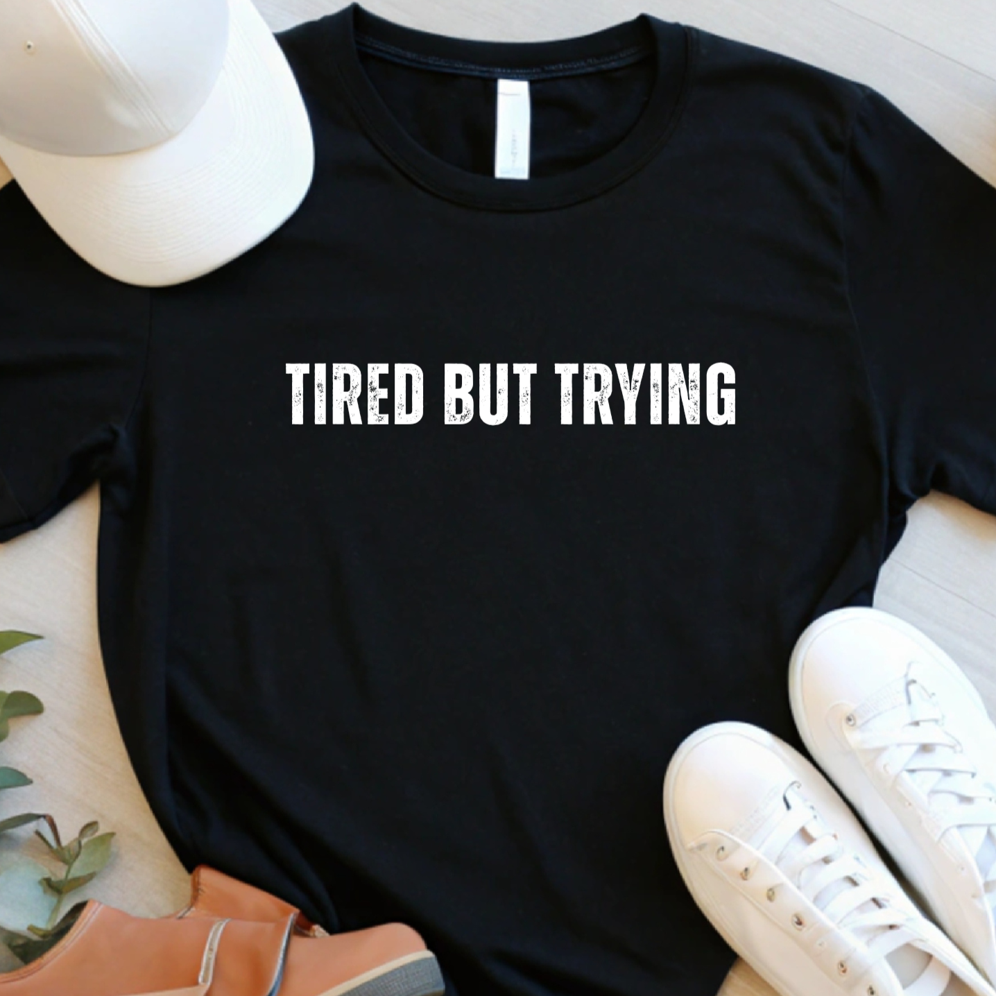 Flat lay of black tired but trying graphic t shirt with centered white text