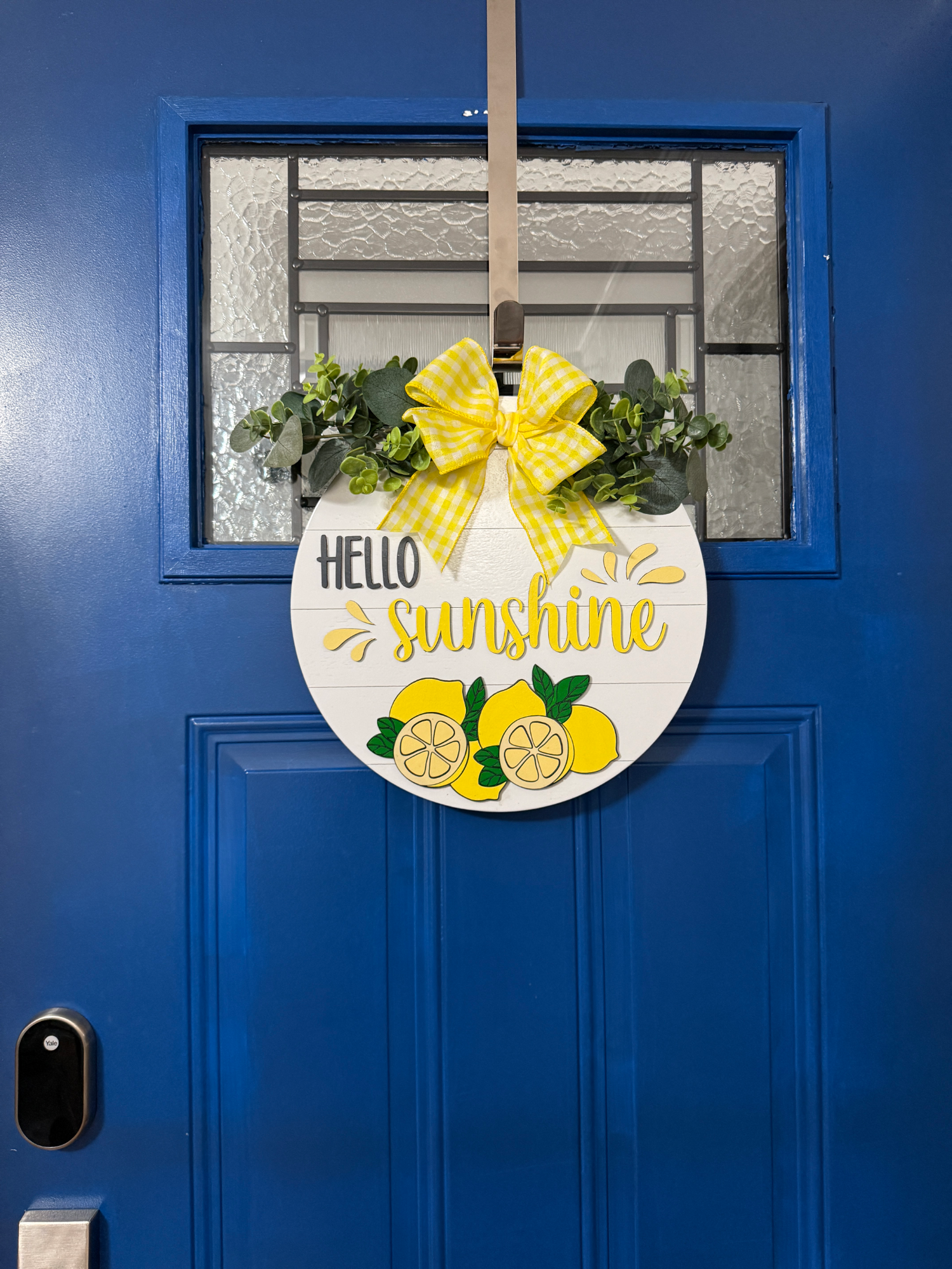 Full view of Hello Sunshine lemon door hanger displayed on bright blue front door with yellow gingham bow