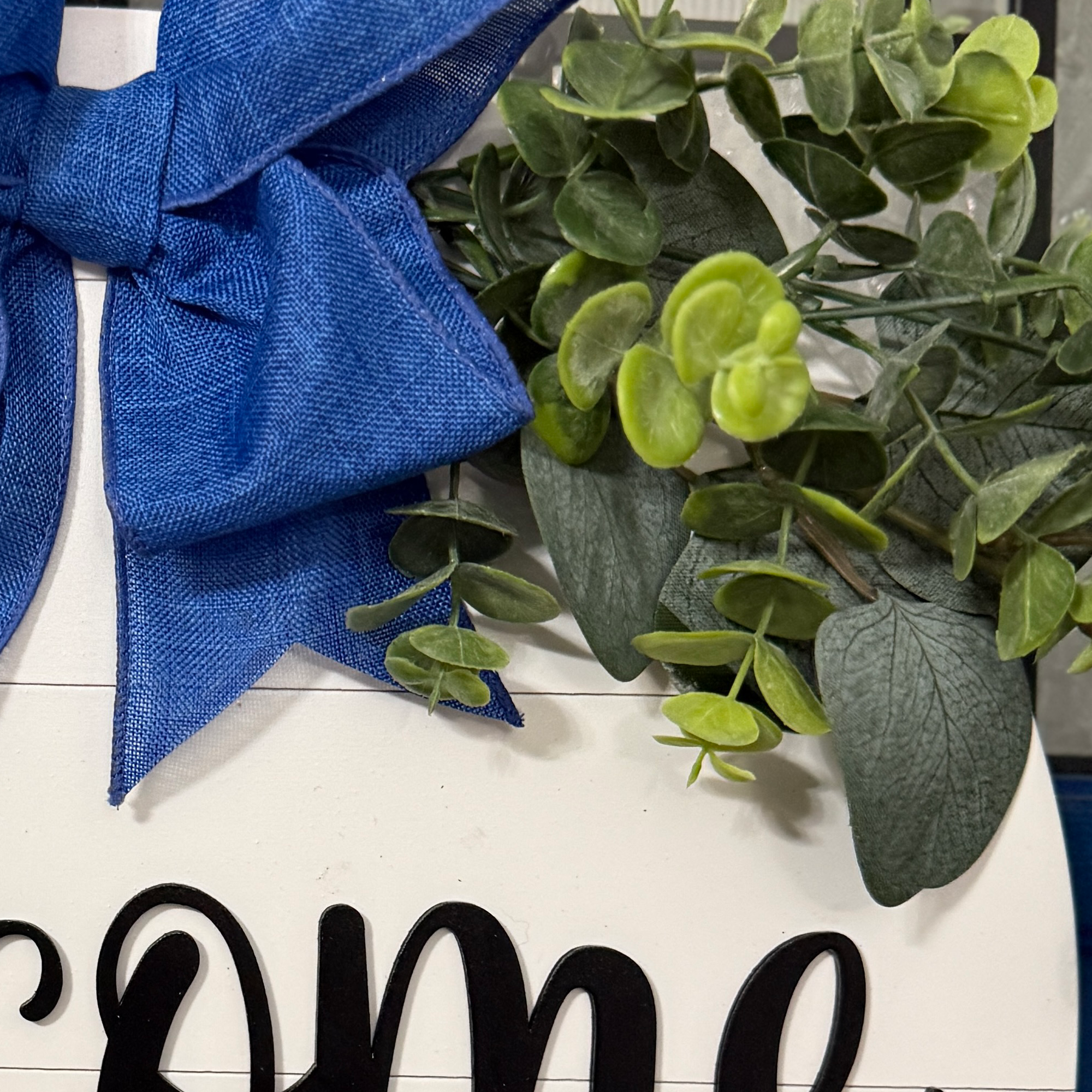 Close-up of greenery and royal blue bow on handcrafted welcome sign