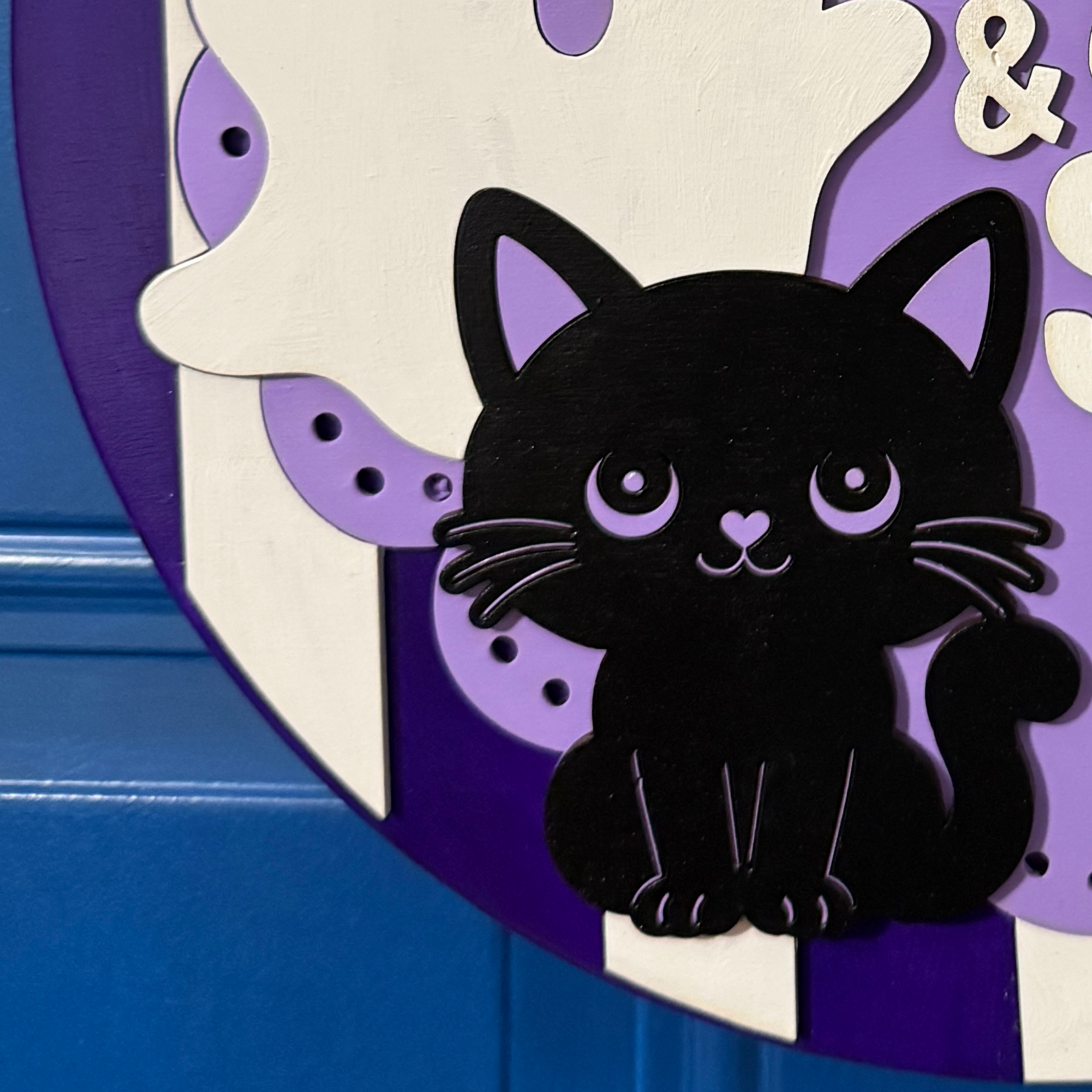 Close-up of dimensional black cat with purple eyes and accents on purple striped Halloween door hanger