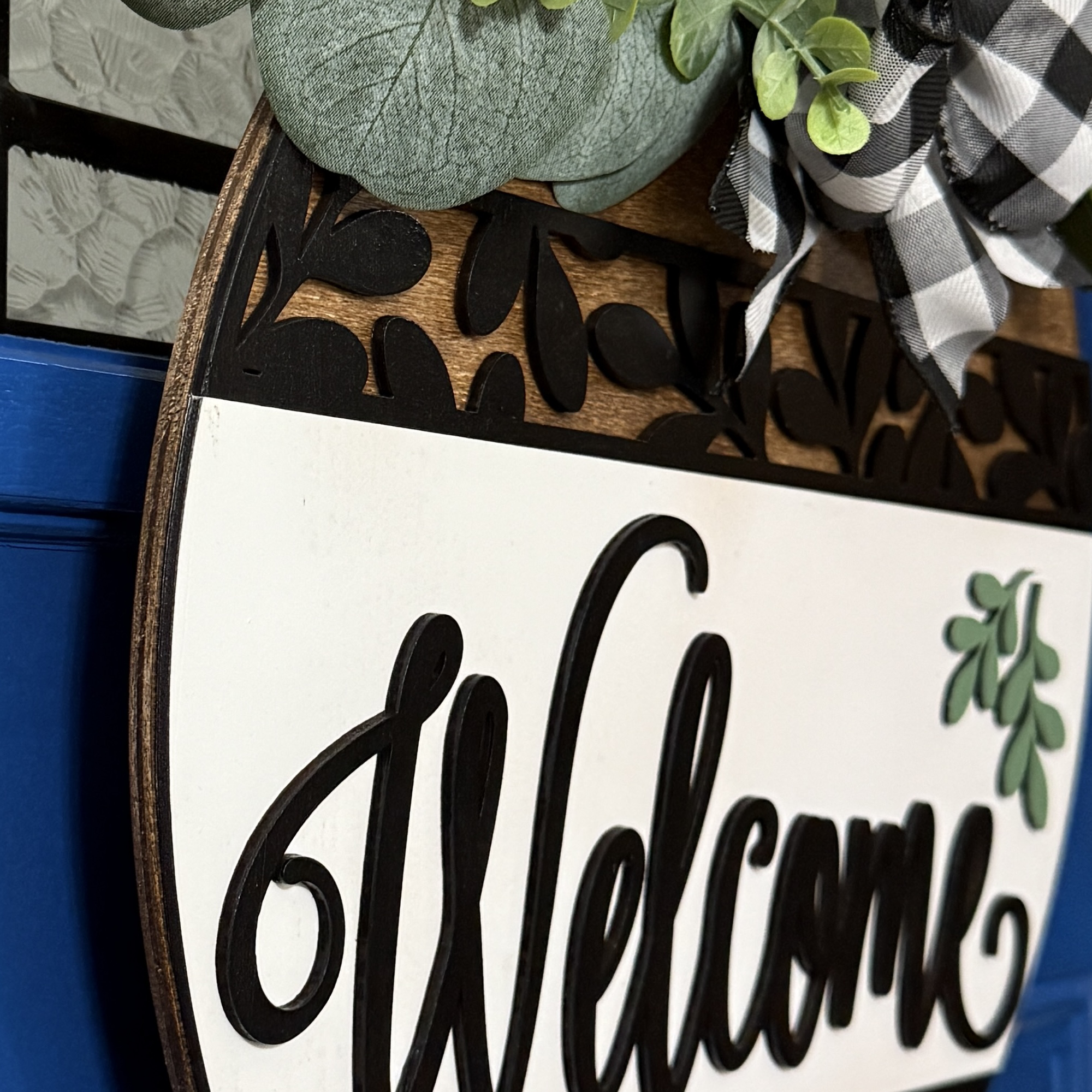 Close-up of “Welcome” script lettering with black cutout leaf accents and faux greenery