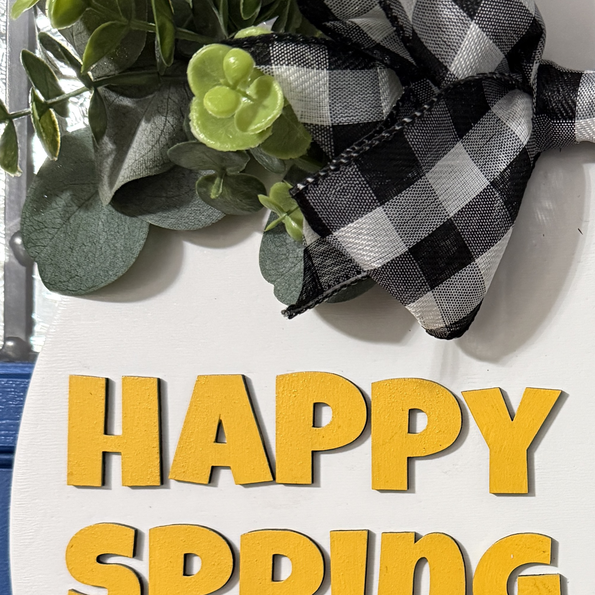 Close-up of greenery and buffalo plaid bow at top of spring door hanger