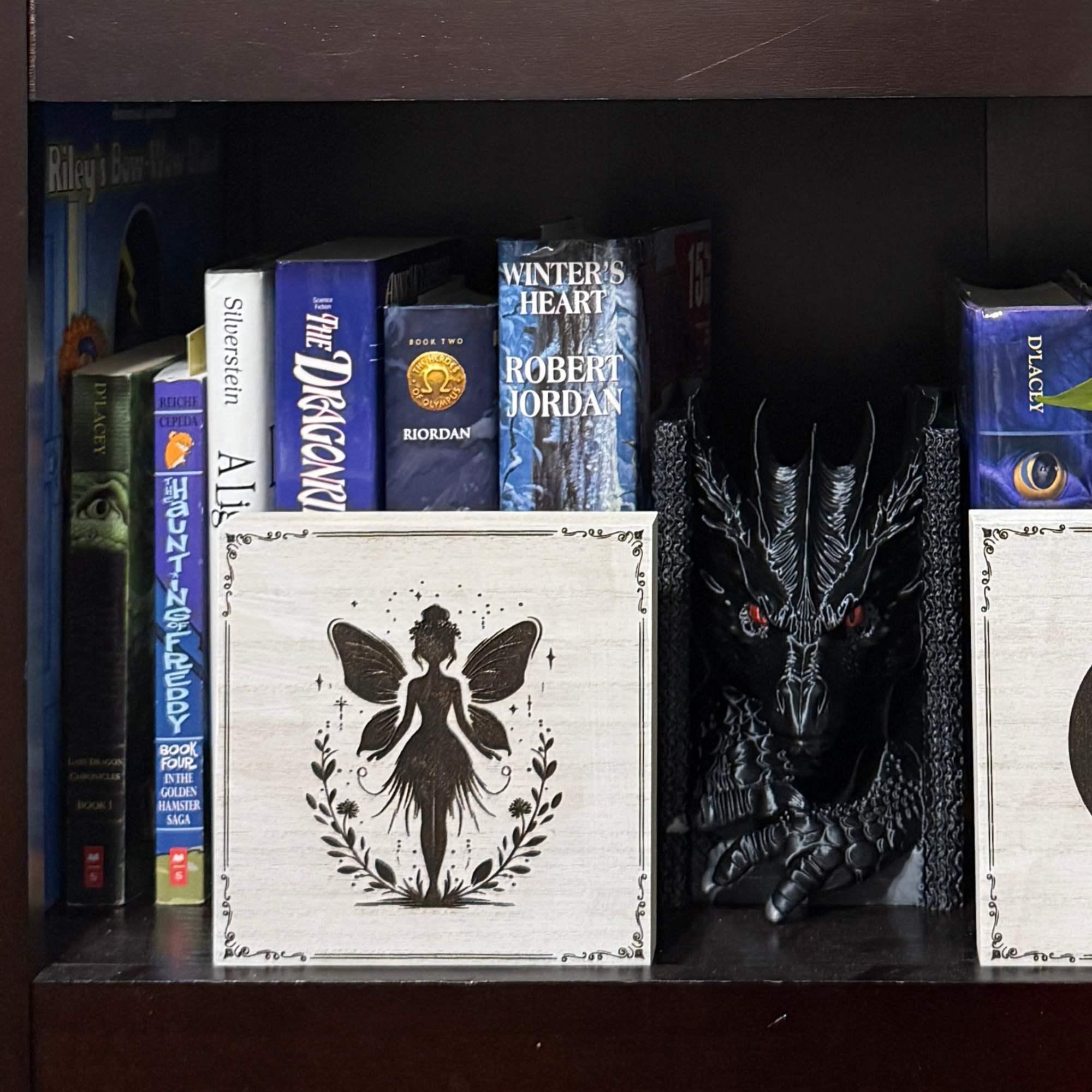Guardian fairy shelf sitter on a bookshelf beside fantasy novels and dragon decor, highlighting engraved fairy artwork
